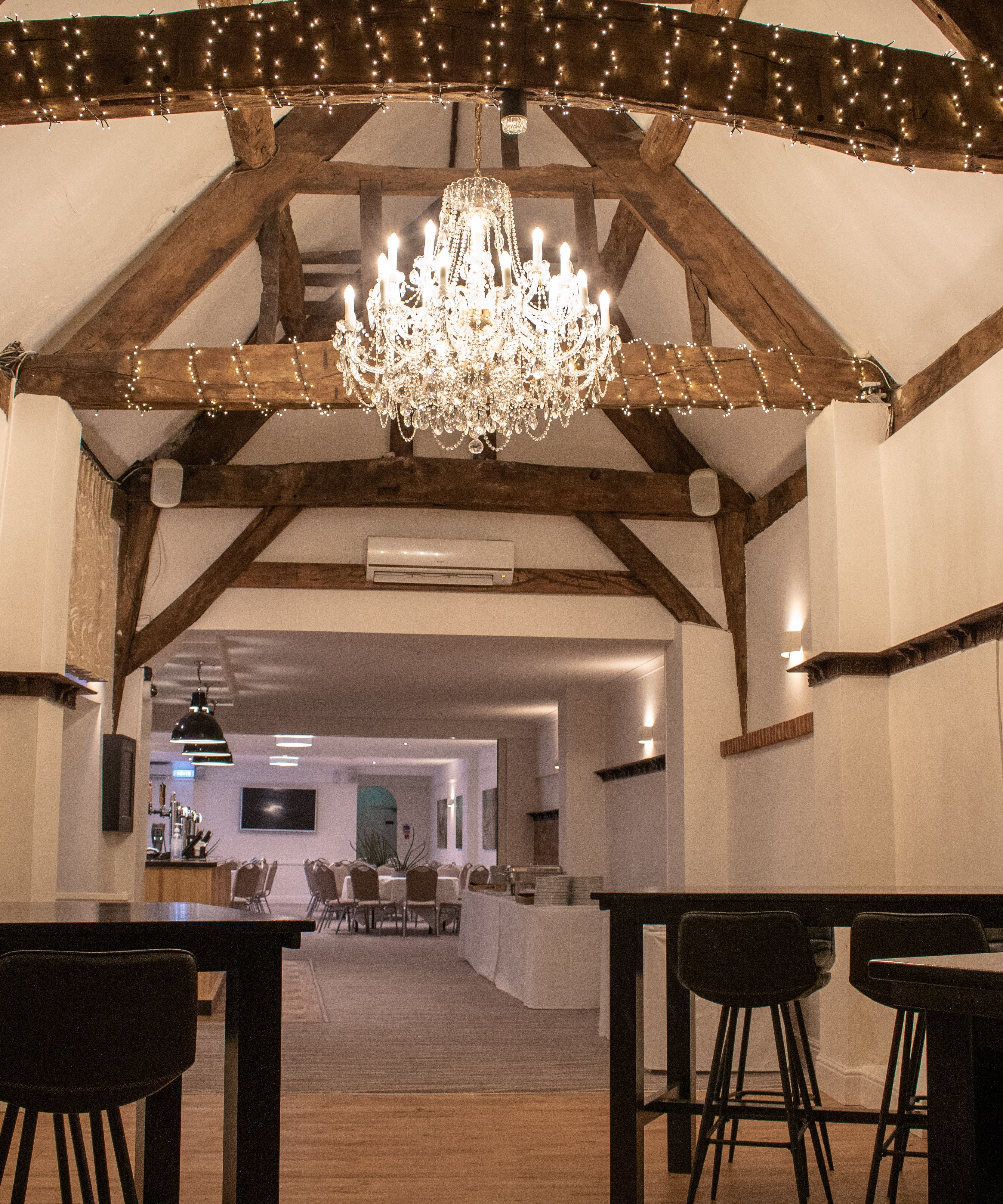 Rustic event space with exposed wooden beams, chandelier, and tables
