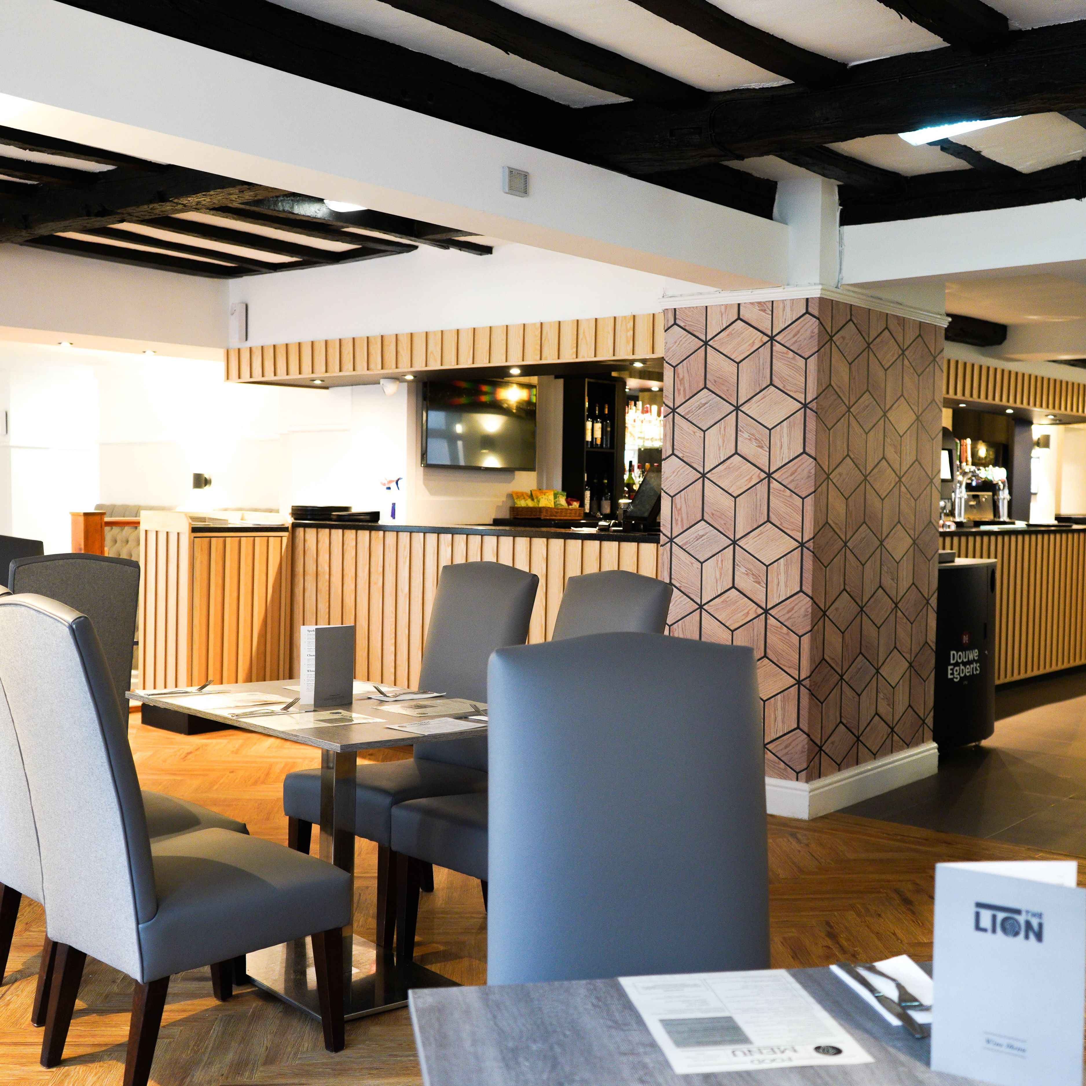 Modern restaurant interior with wooden flooring, grey chairs, and a geometric accent wall.