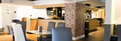 Modern restaurant interior with wooden flooring, grey chairs, and a geometric accent wall.