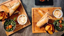 Assorted sandwiches served with potato wedges, coleslaw, and fresh salad on wooden boards.