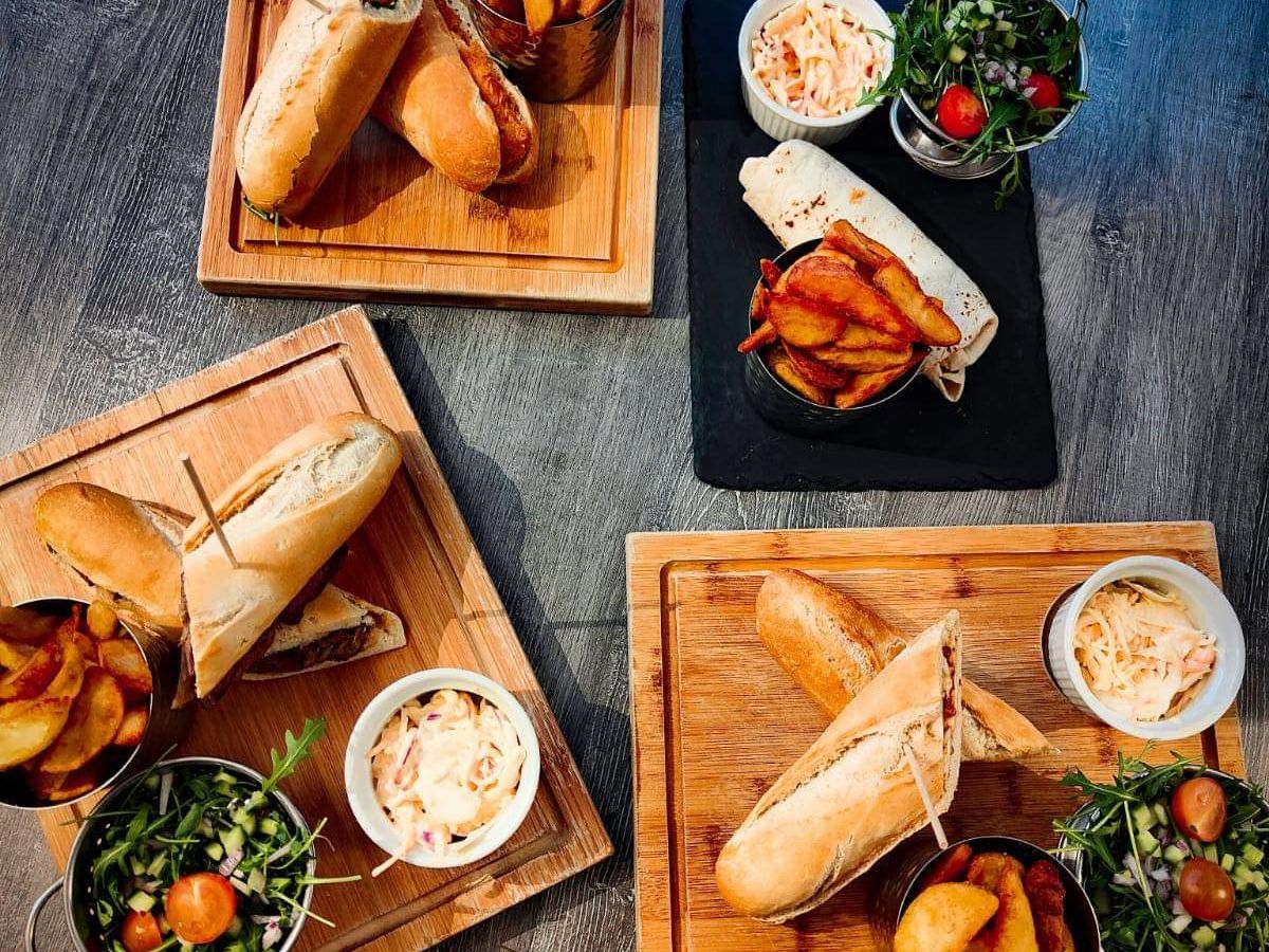 Assorted sandwiches served with potato wedges, coleslaw, and fresh salad on wooden boards.