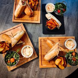 Assorted sandwiches served with potato wedges, coleslaw, and fresh salad on wooden boards.