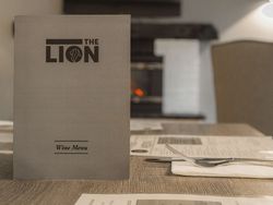 Wine menu card standing on a table with food menus and cutlery in a restaurant setting.