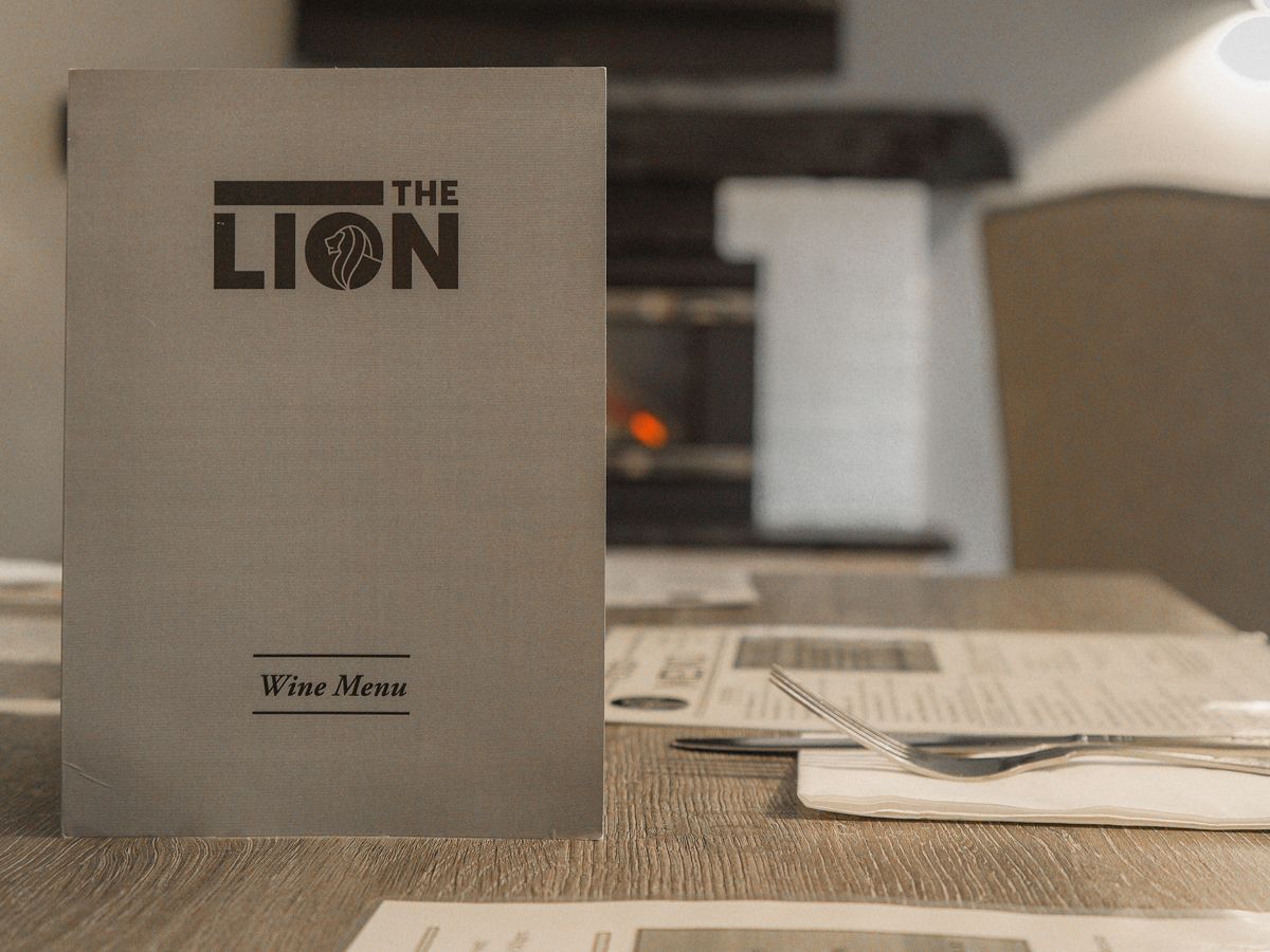 Wine menu card standing on a table with food menus and cutlery in a restaurant setting.