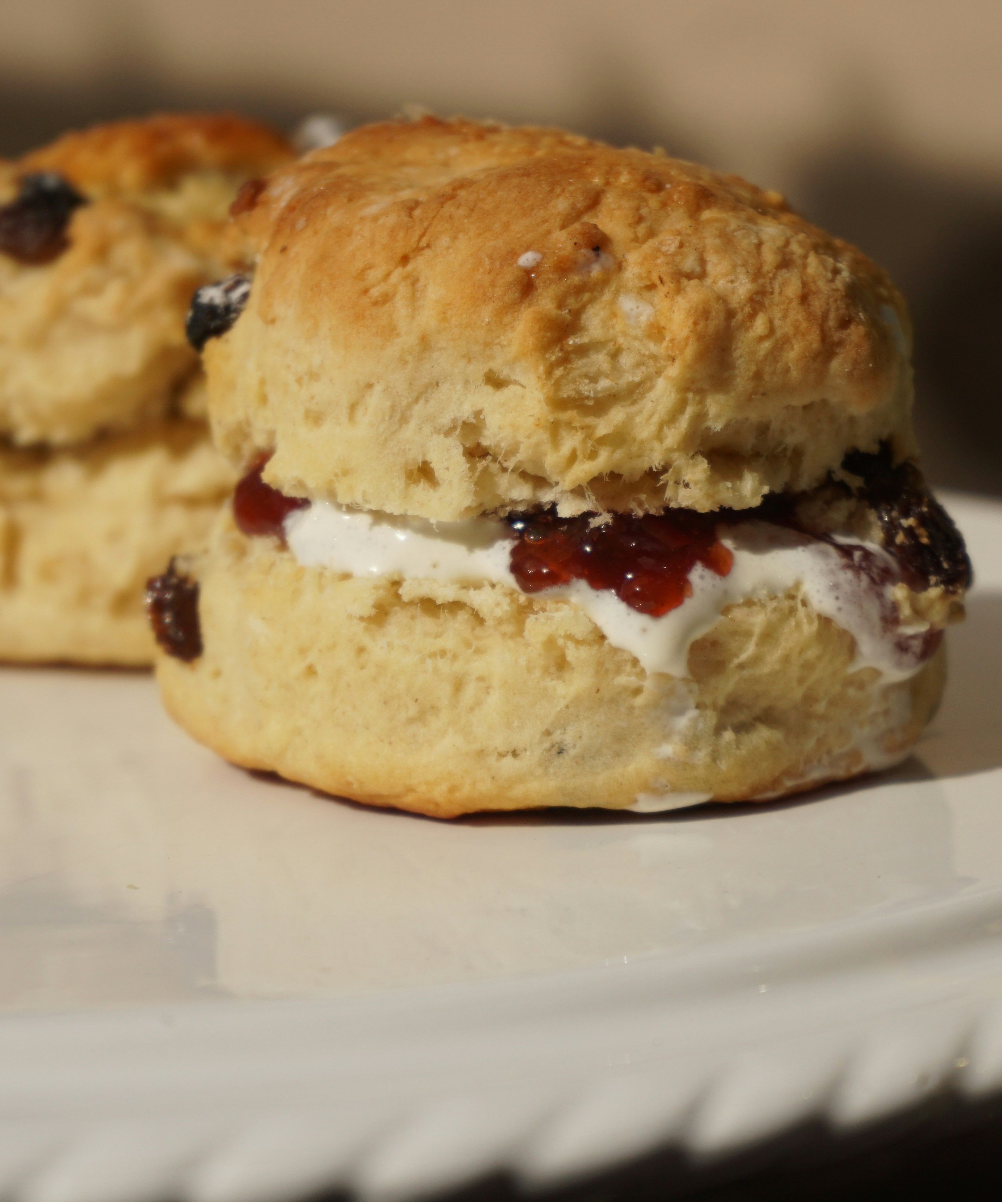 Two scones with raisins filled with clotted cream and jam on a white plate