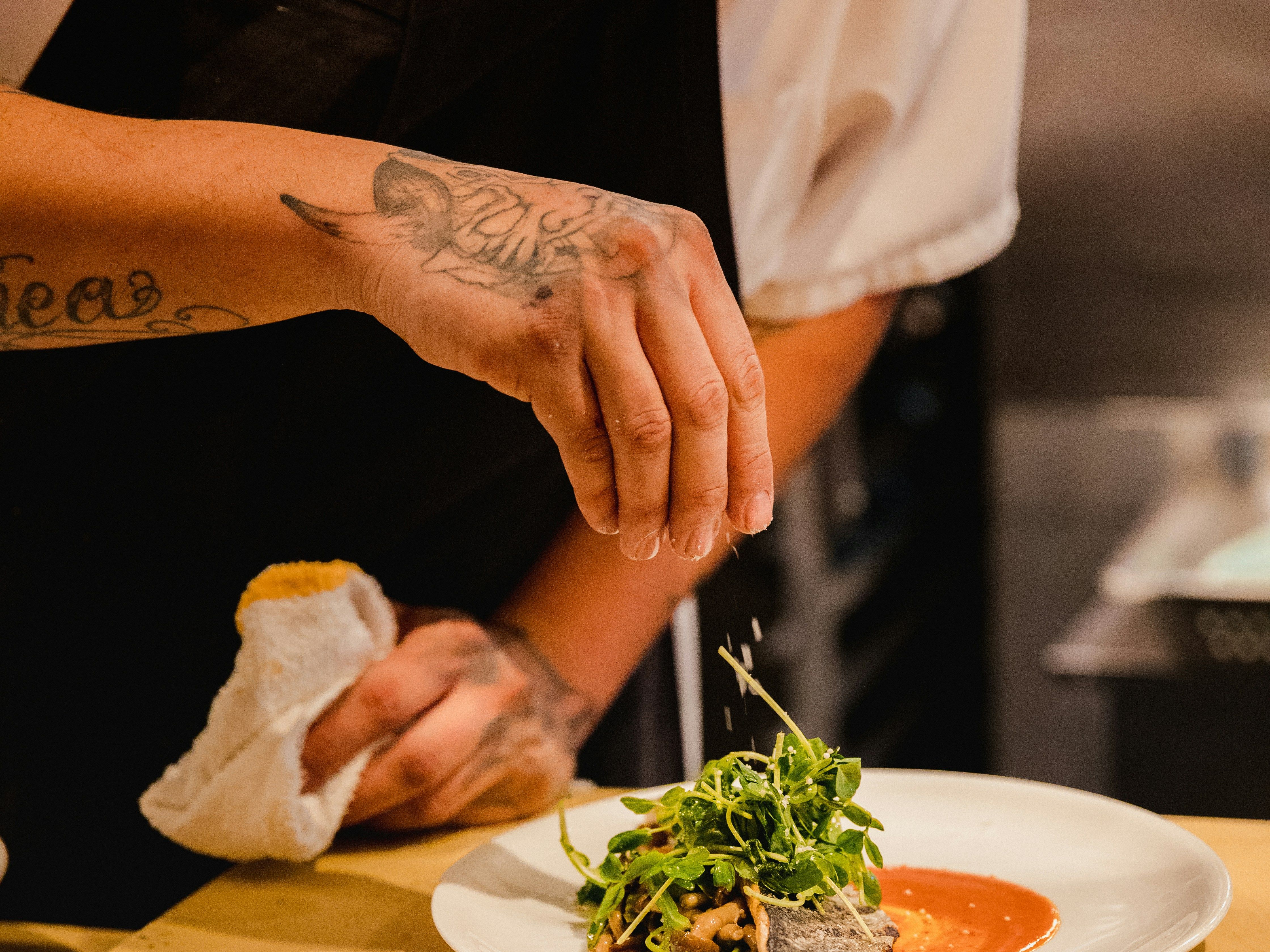 Chef garnishing a plated dish with fresh greens in a restaurant kitchen