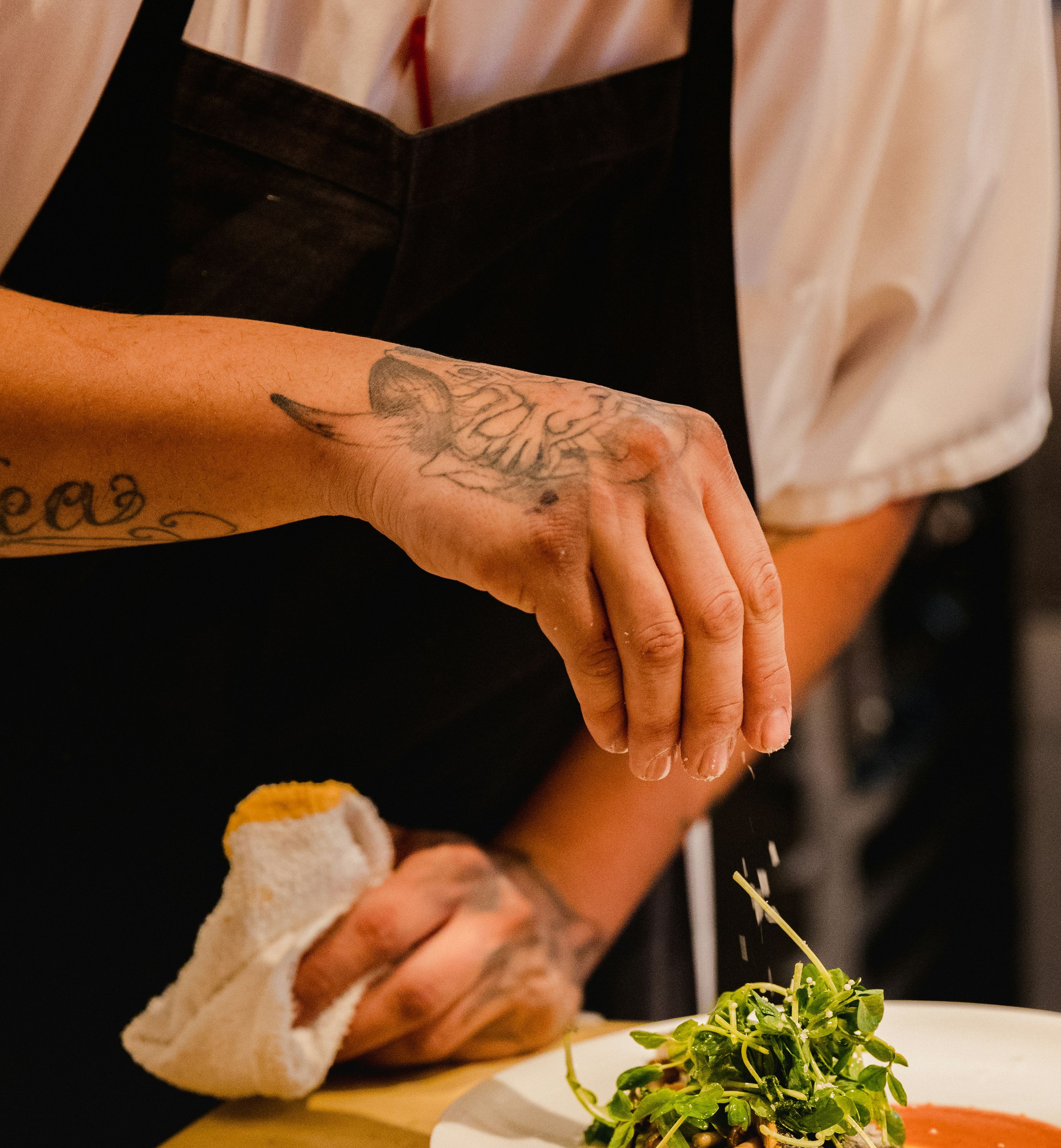 Chef garnishing a plated dish with fresh greens in a restaurant kitchen