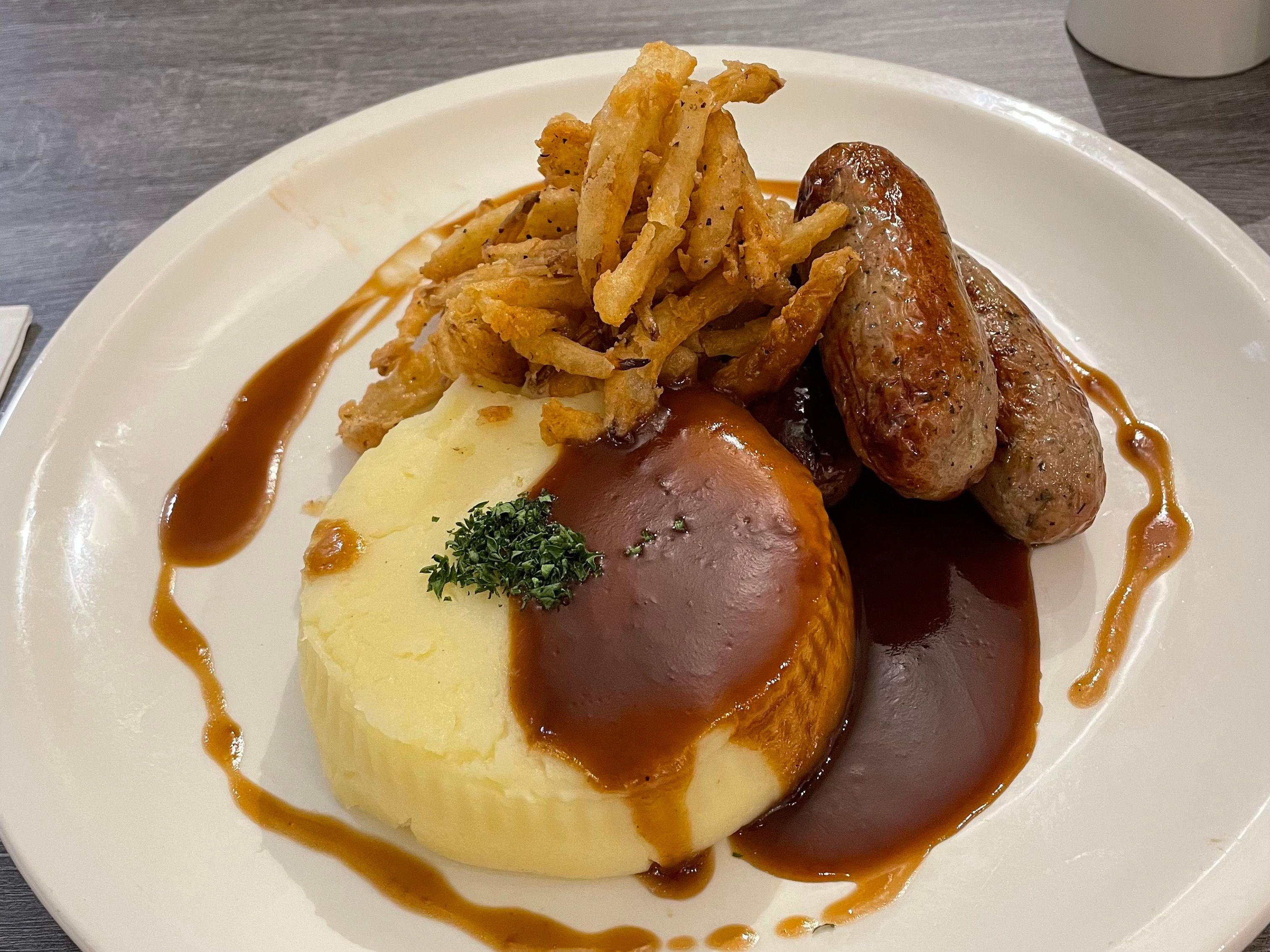 A plate with mashed potatoes, sausages, crispy fried onions, and brown gravy.