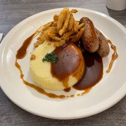 A plate with mashed potatoes, sausages, crispy fried onions, and brown gravy.