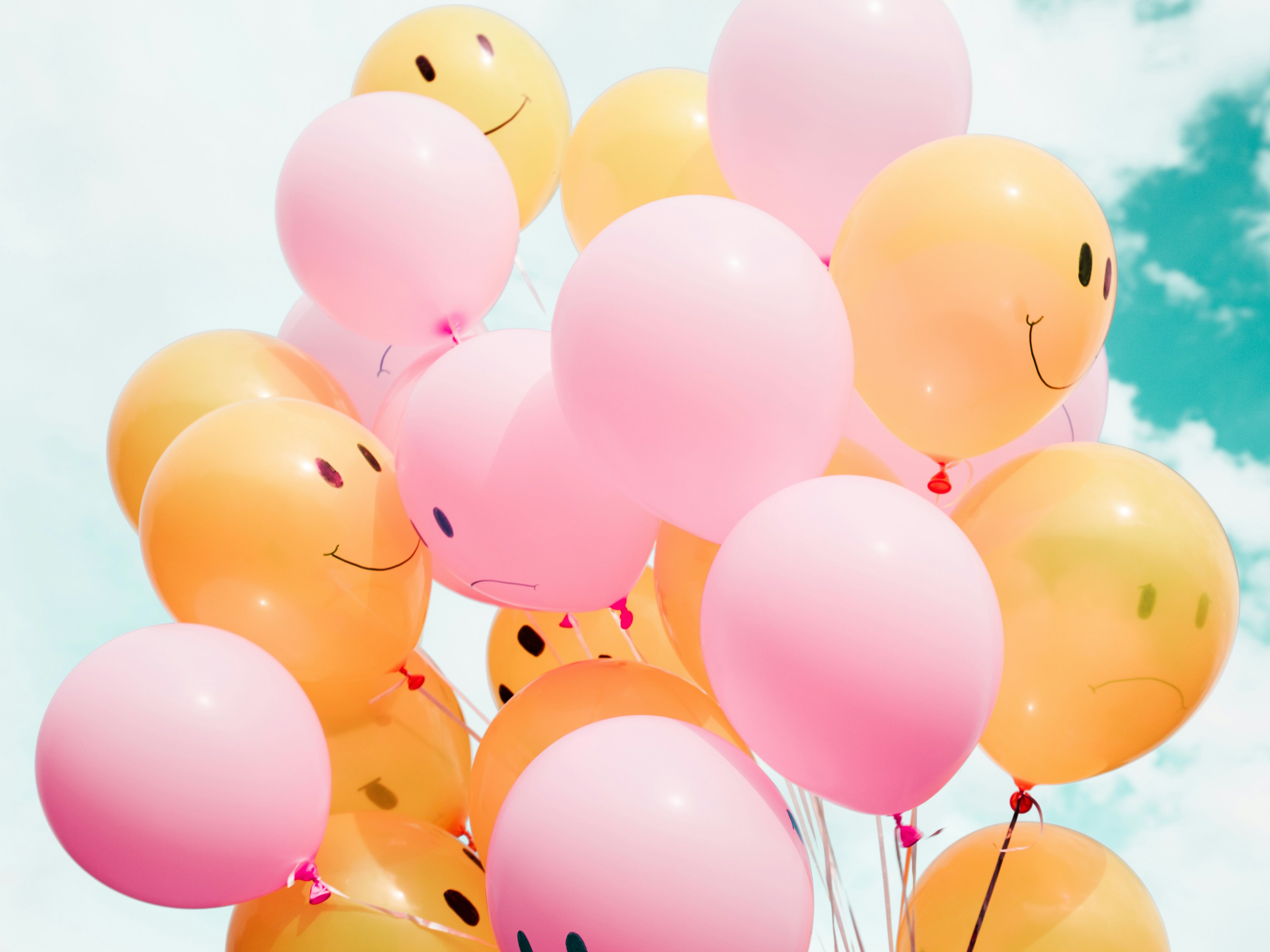Pink and yellow balloons with smiley and sad faces drawn on them floating against a blue sky