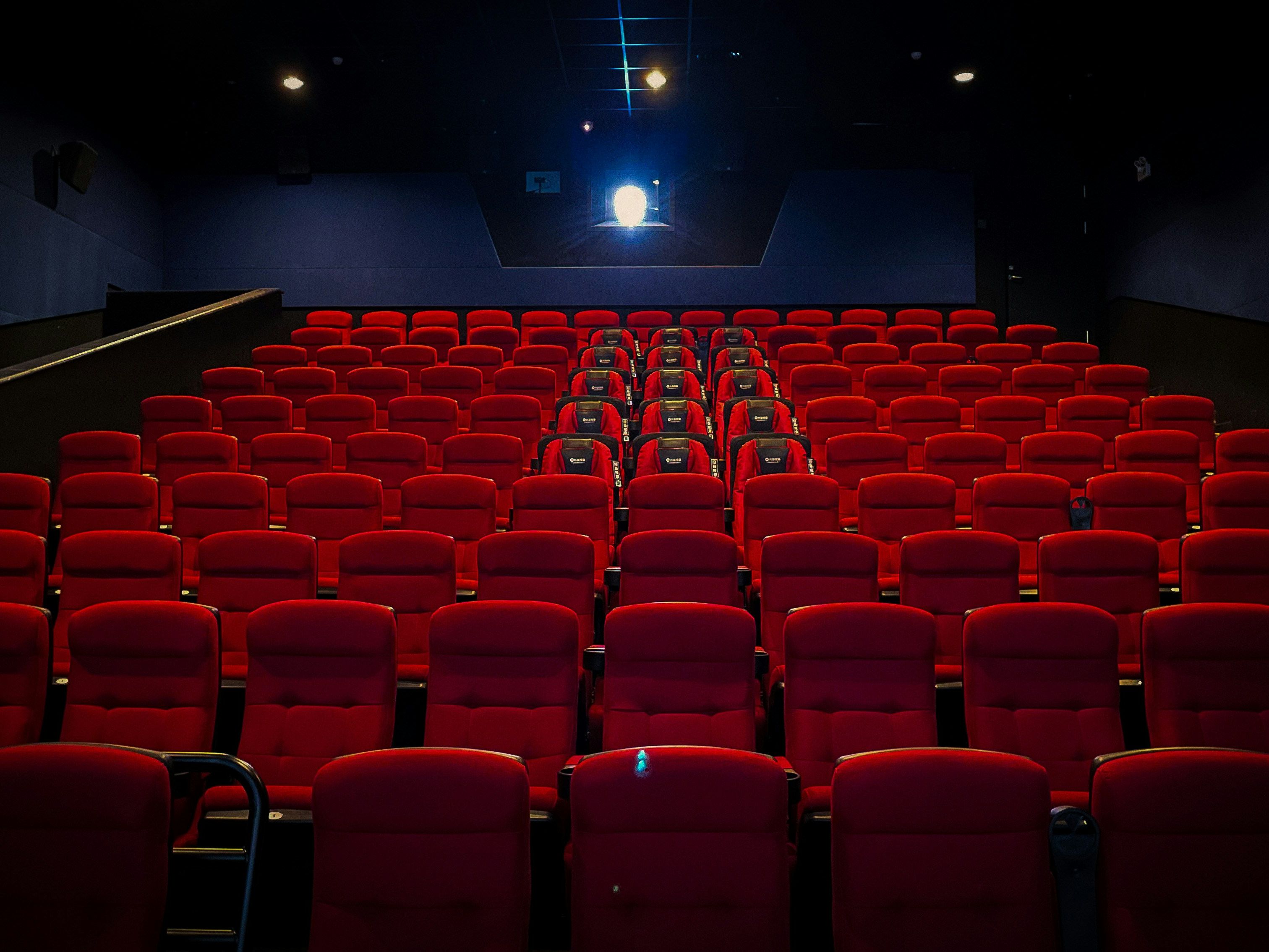 Empty cinema hall with rows of red seats and a lit projector at the back
