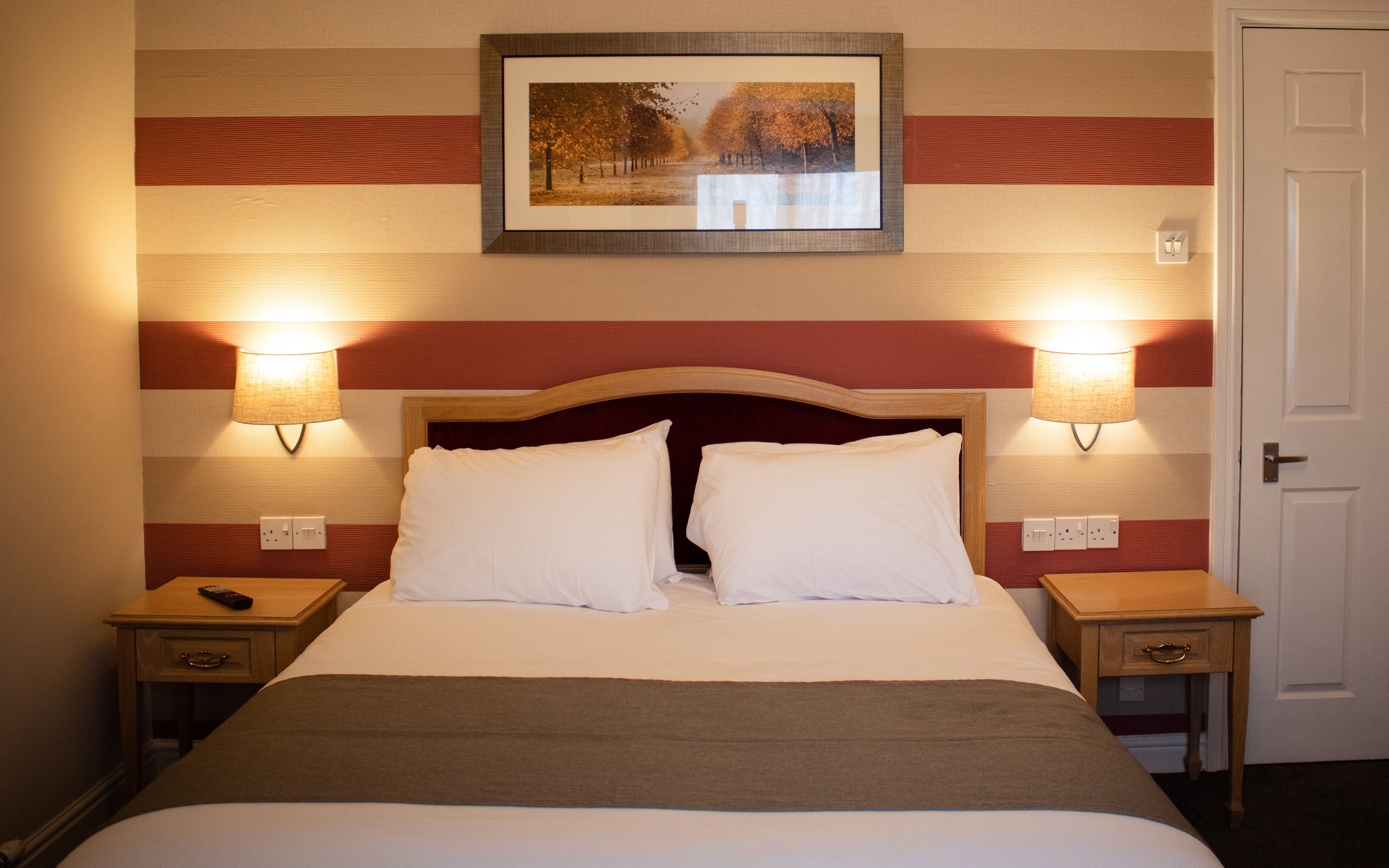 A cozy hotel family room with a double bed, striped wallpaper, bedside tables, and warm lighting.