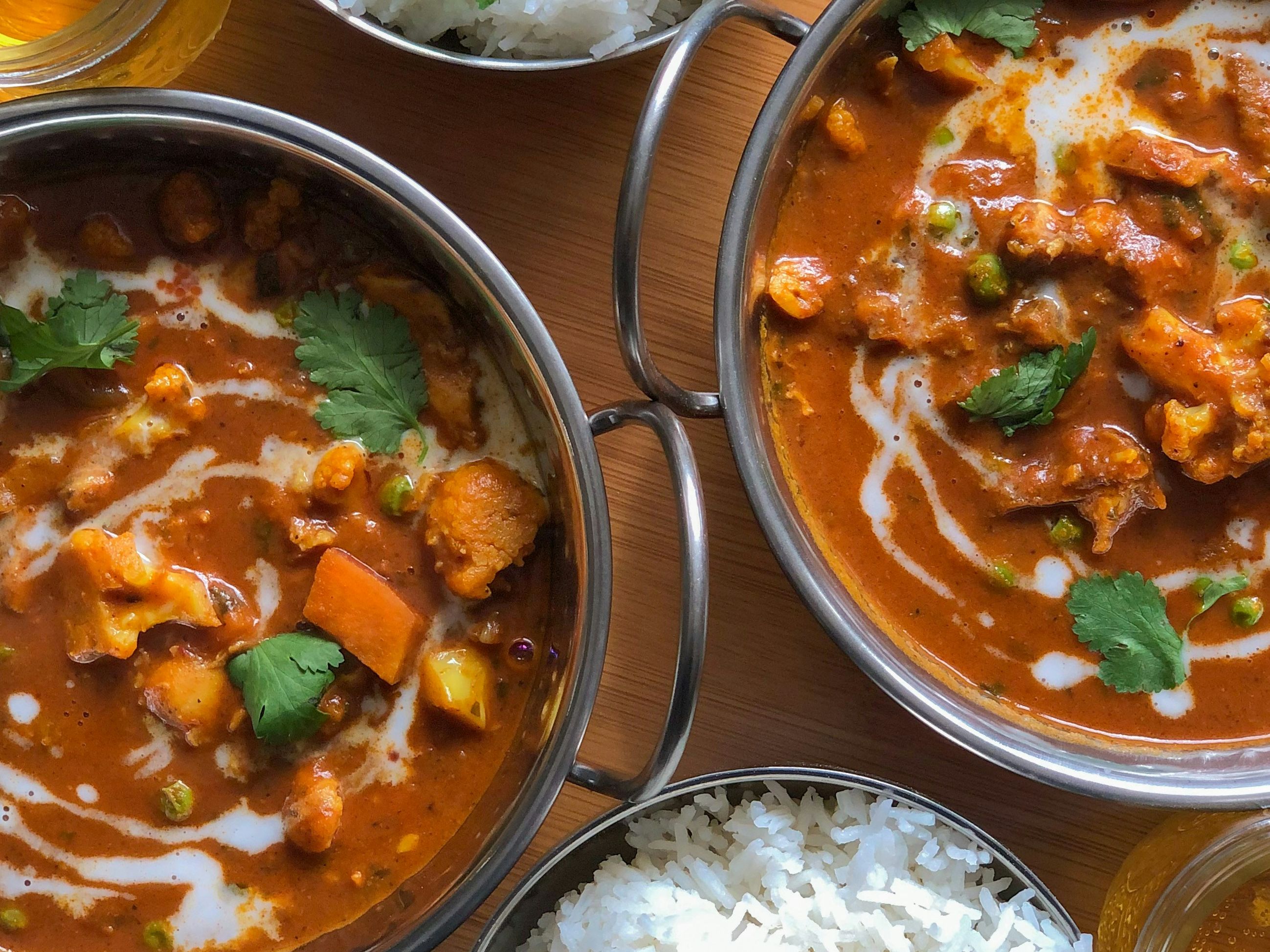 Indian curry dishes with white rice and drinks on a wooden tray