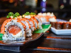 Close-up of assorted sushi rolls on a dark plate with fresh ingredients and garnishes.