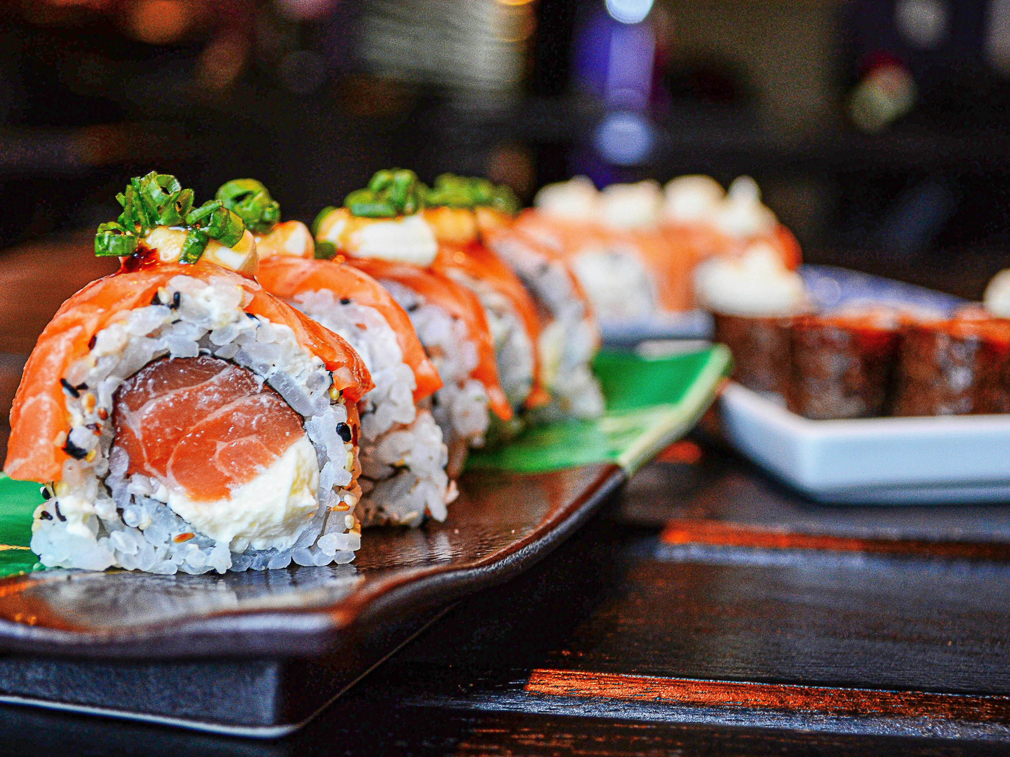 Close-up of assorted sushi rolls on a dark plate with fresh ingredients and garnishes.