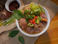 Vietnamese noodle soup with beef and herbs in a white bowl, garnished with fresh greens and sliced chili peppers.