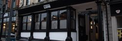 Street view of The Lion pub entrance on Bridge Street with black and white exterior, large windows, and a hanging sign.