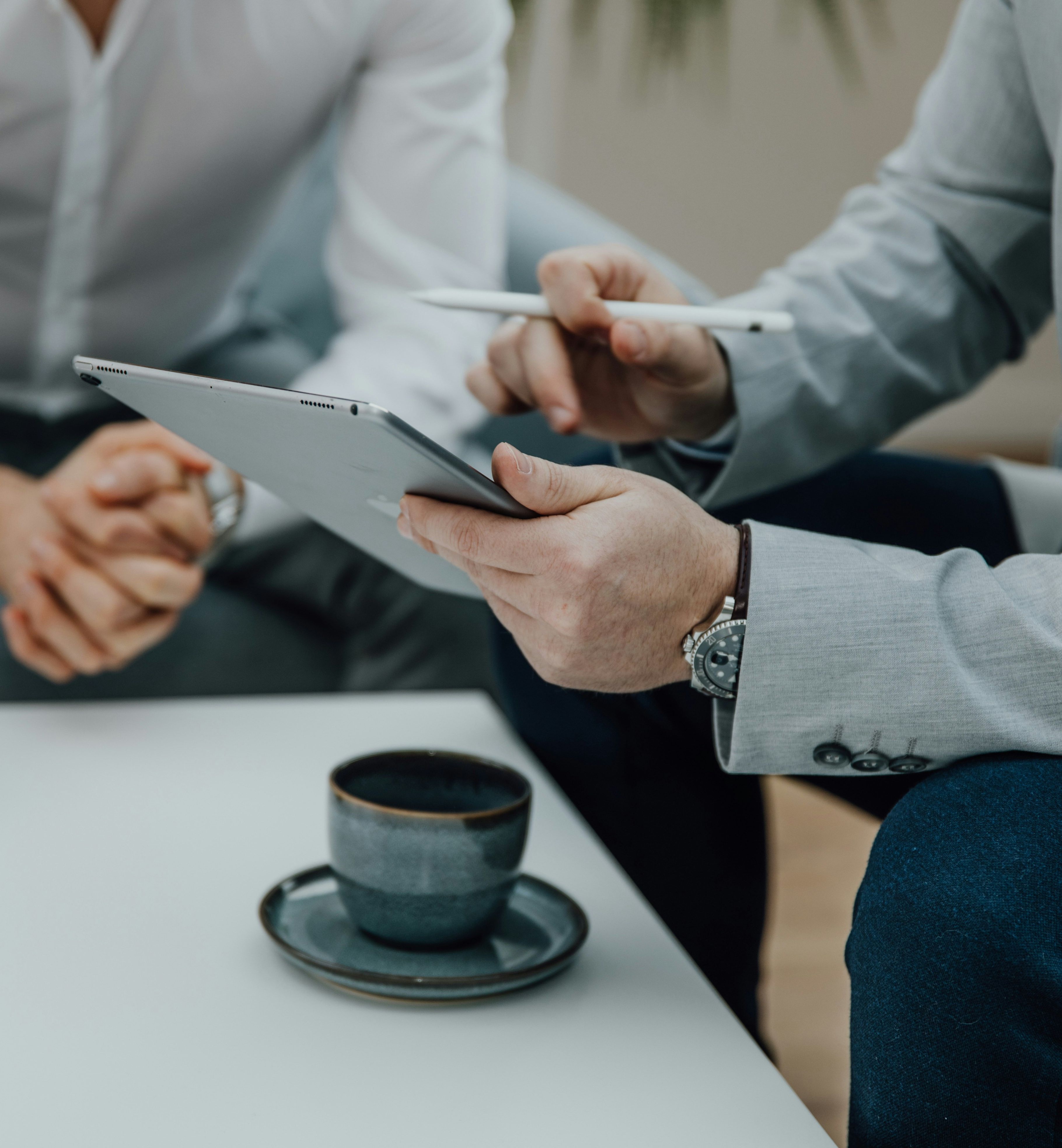 Two businessmen discussing something while looking at a tablet, with coffee cups on the table.
