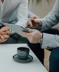 Two businessmen discussing something while looking at a tablet, with coffee cups on the table.