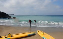 A young girl surfing in the ocean, participating in a surfing lesson at Poldhu Beach.