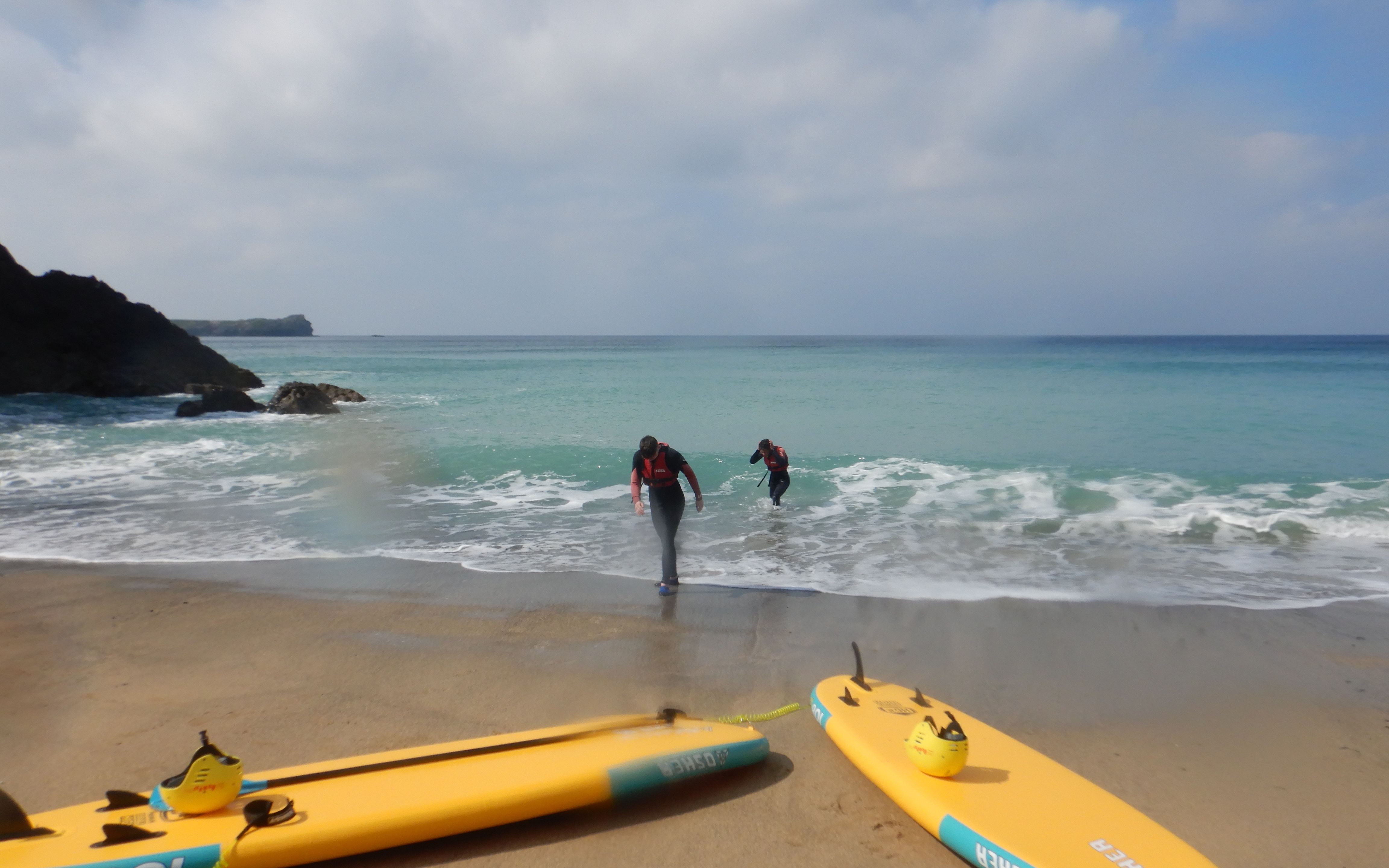 A young girl surfing in the ocean, participating in a surfing lesson at Poldhu Beach.