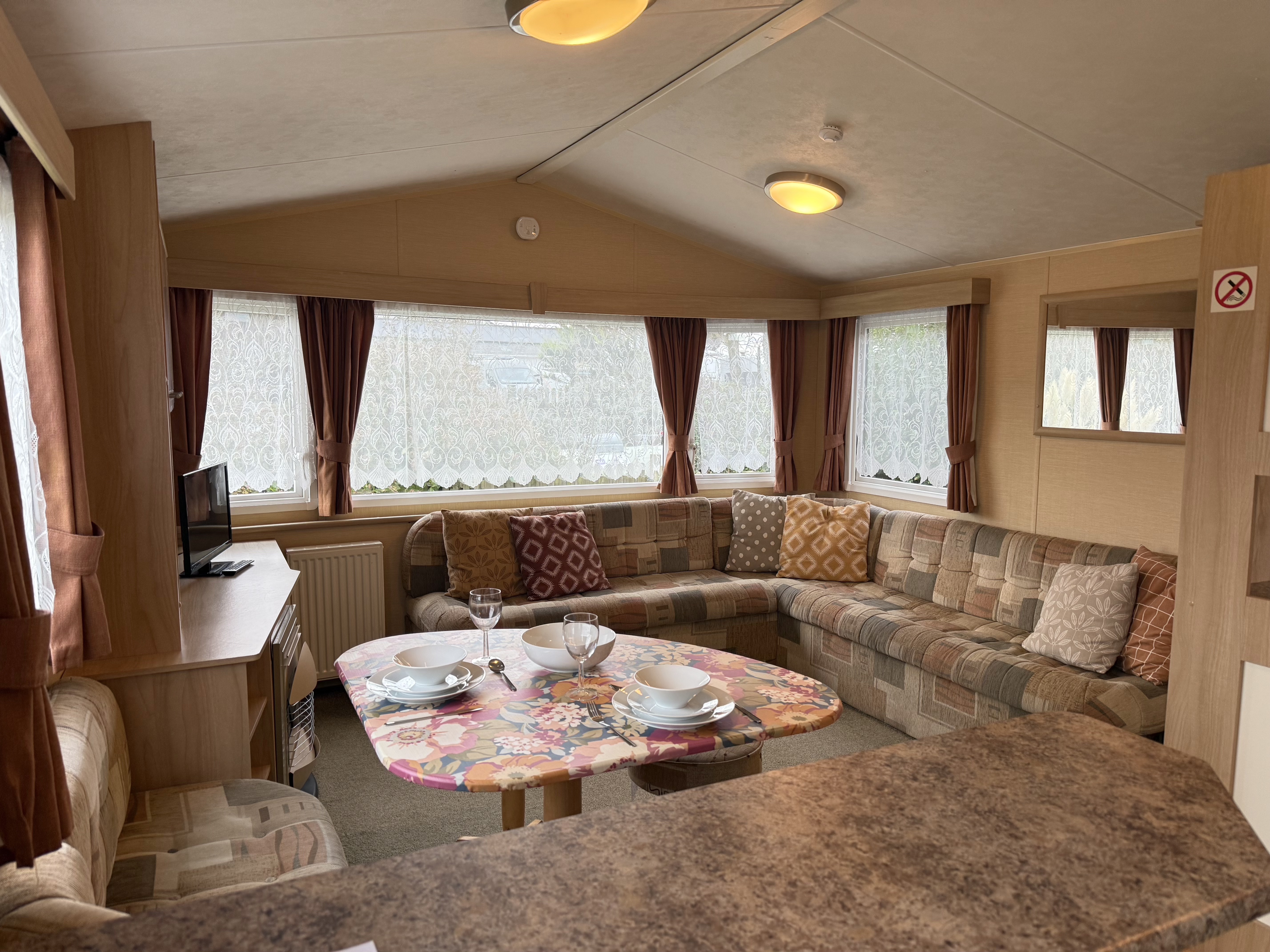 Interior of a cozy caravan living space with patterned sofas, a small dining table, and a television.