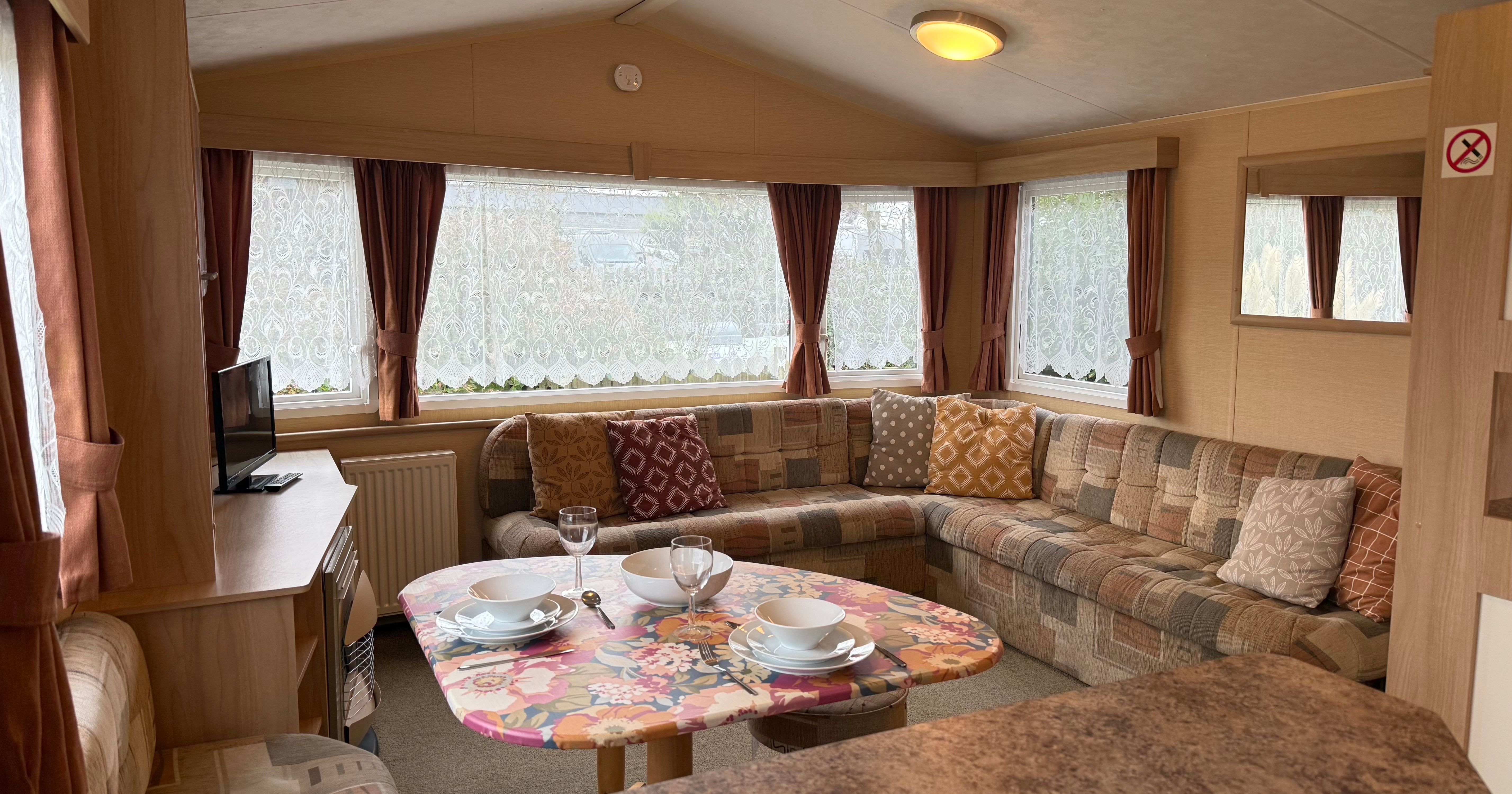 Interior of a cozy caravan living space with patterned sofas, a small dining table, and a television.