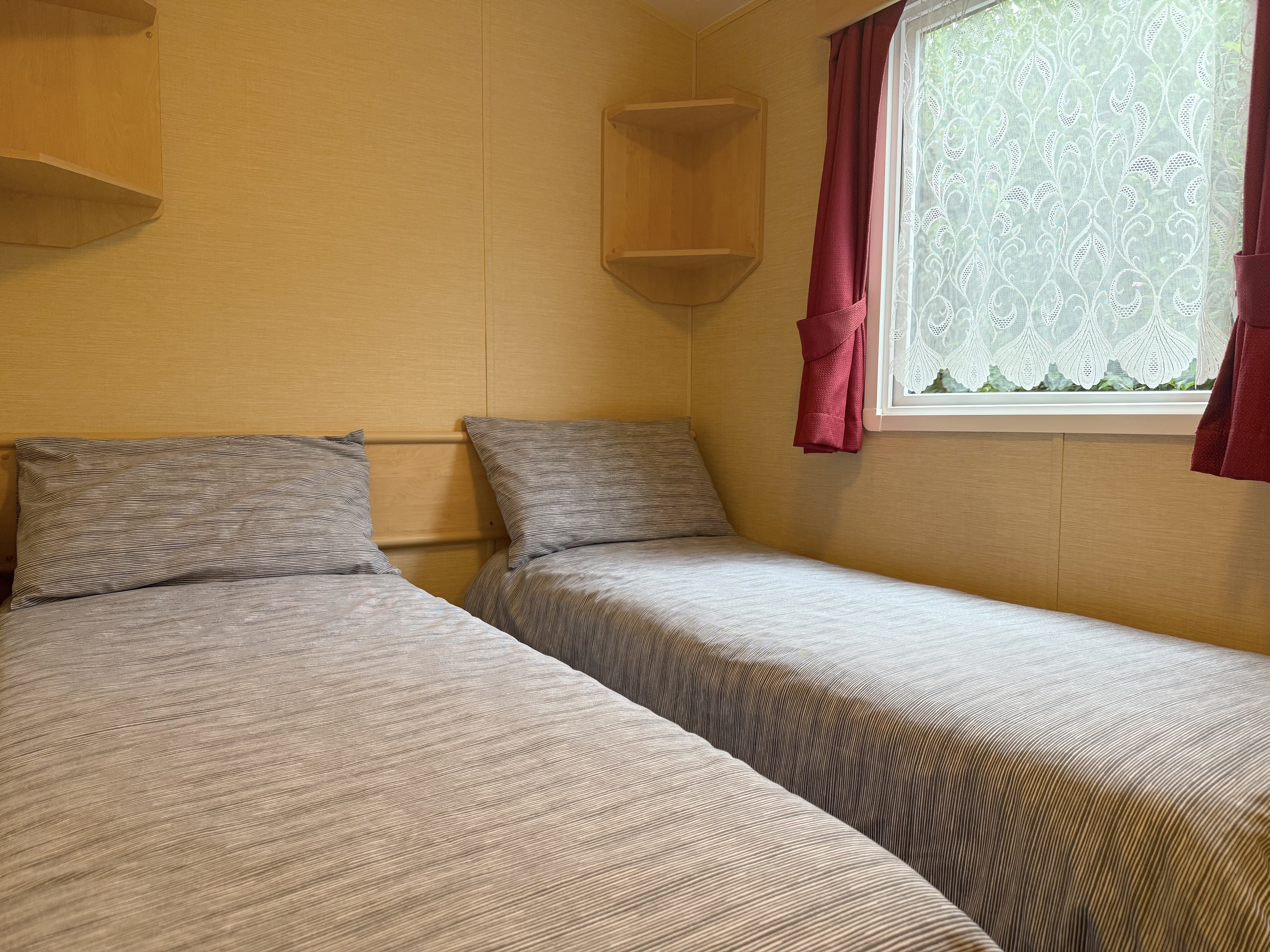 Two single beds with gray bedding in a small room with a window and red curtains