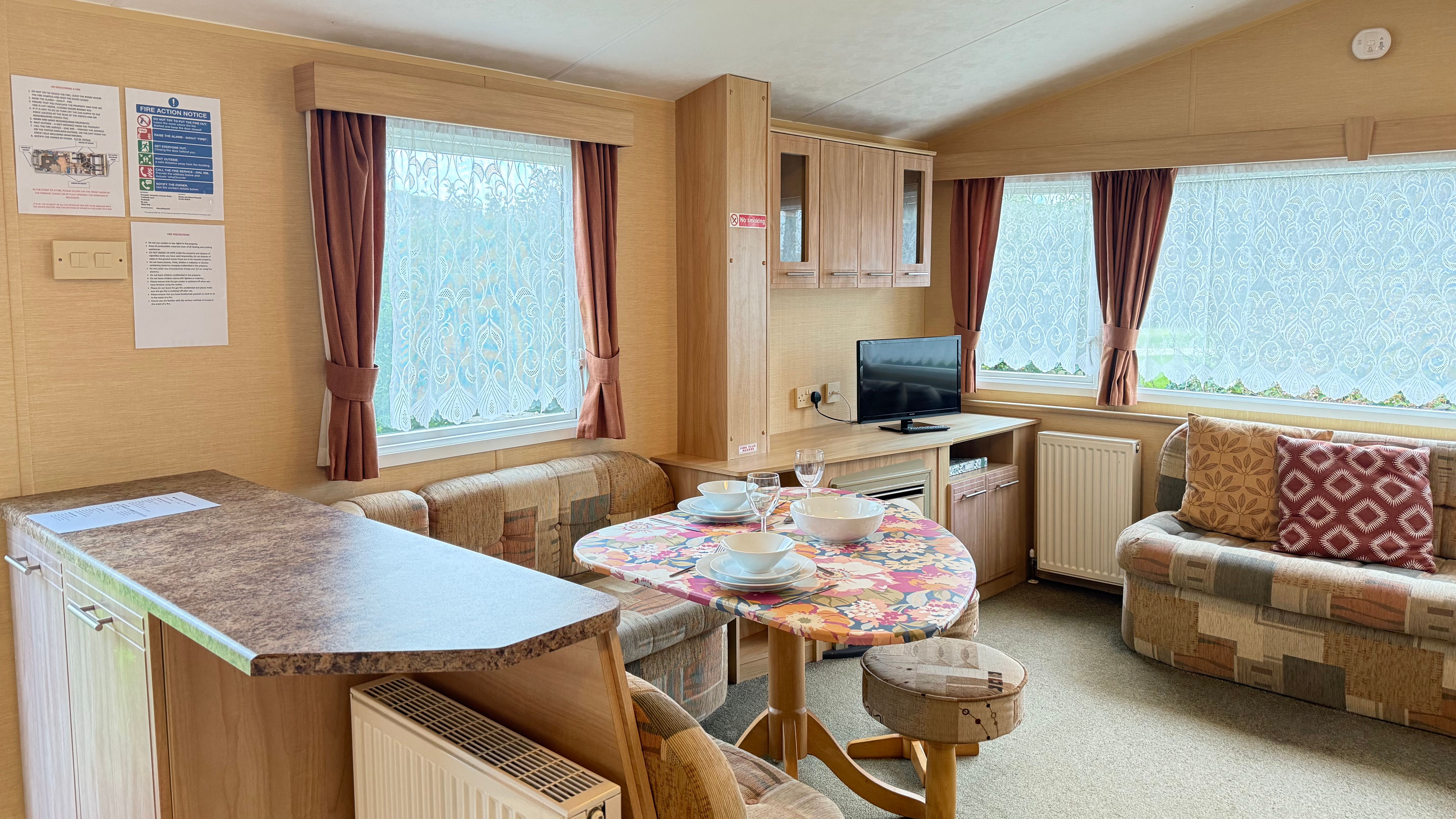 Interior of a cozy caravan living area with a small dining table, television, and sofas.