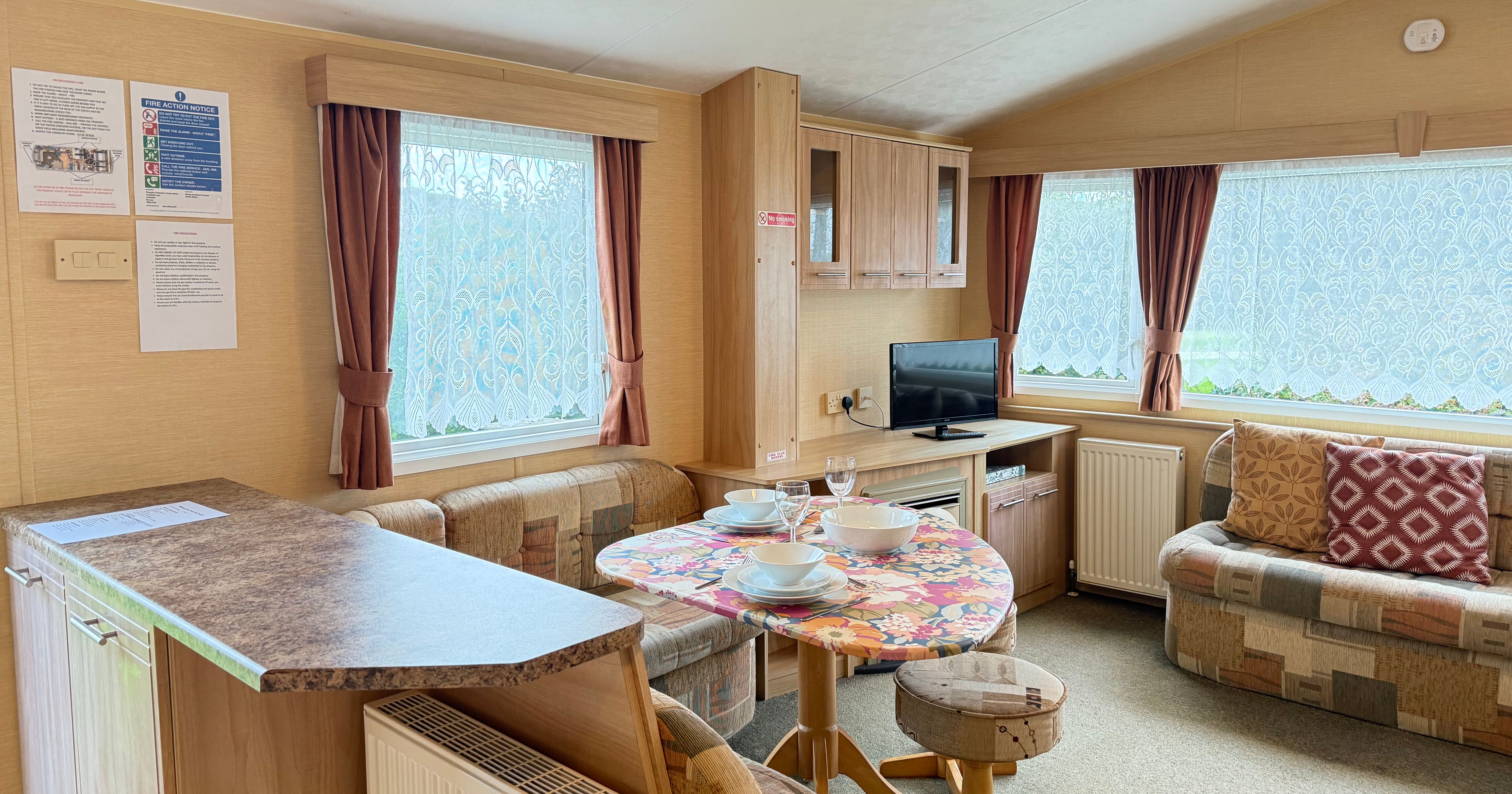 Interior of a cozy caravan living area with a small dining table, television, and sofas.
