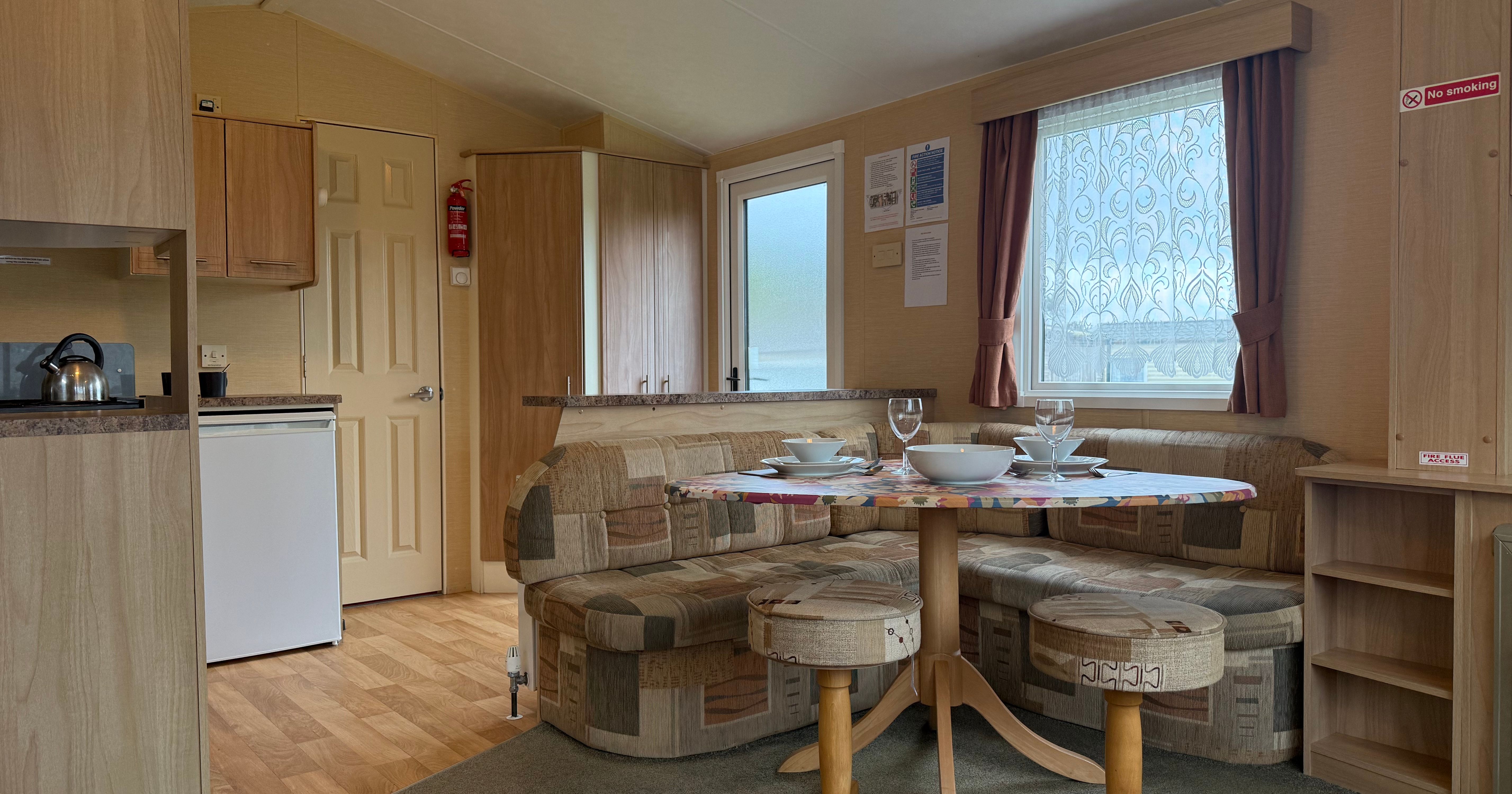 Interior of a cozy mobile home with a small dining area, kitchenette, and seating.