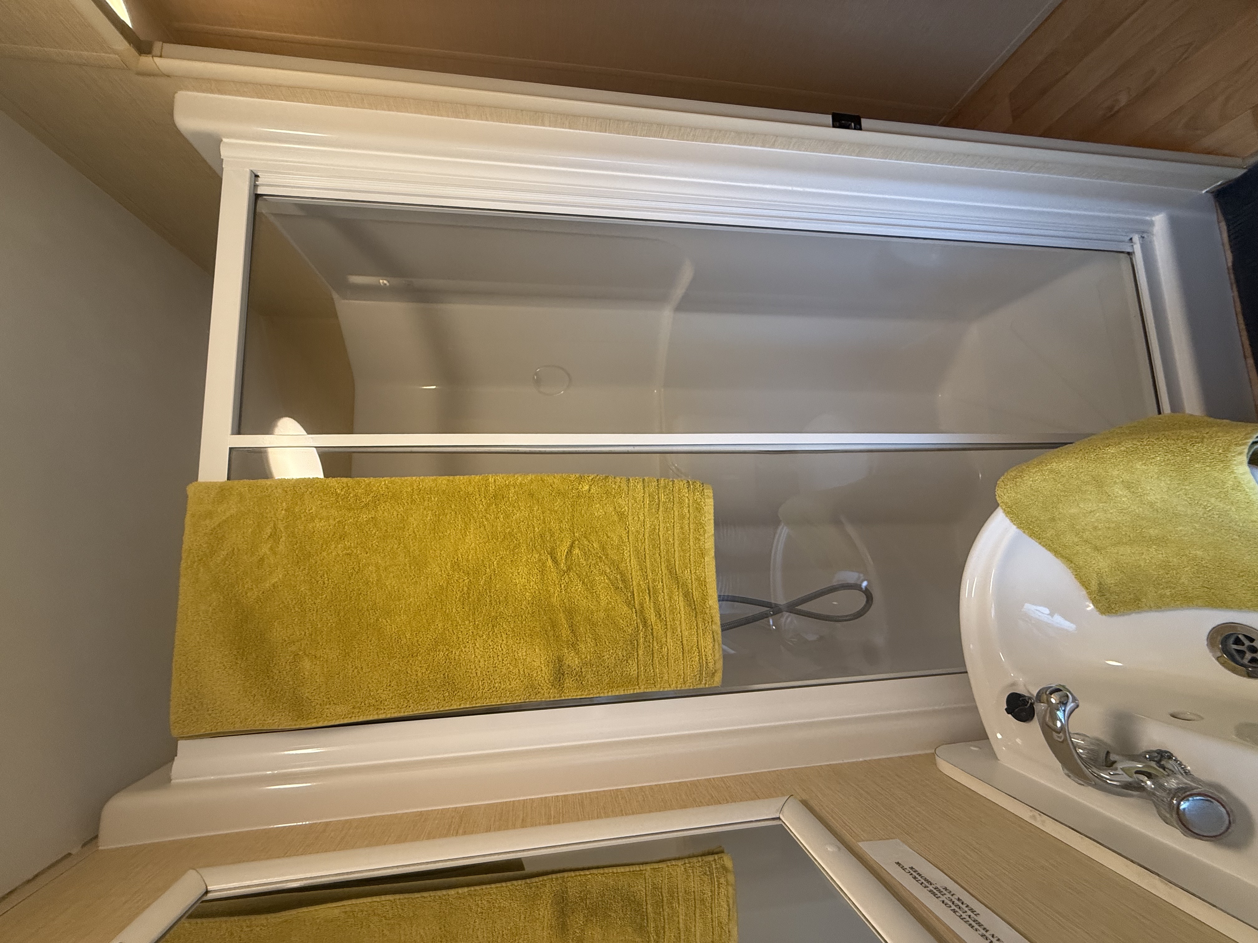 Small bathroom with yellow towels, a shower cabin with glass doors, and a white sink