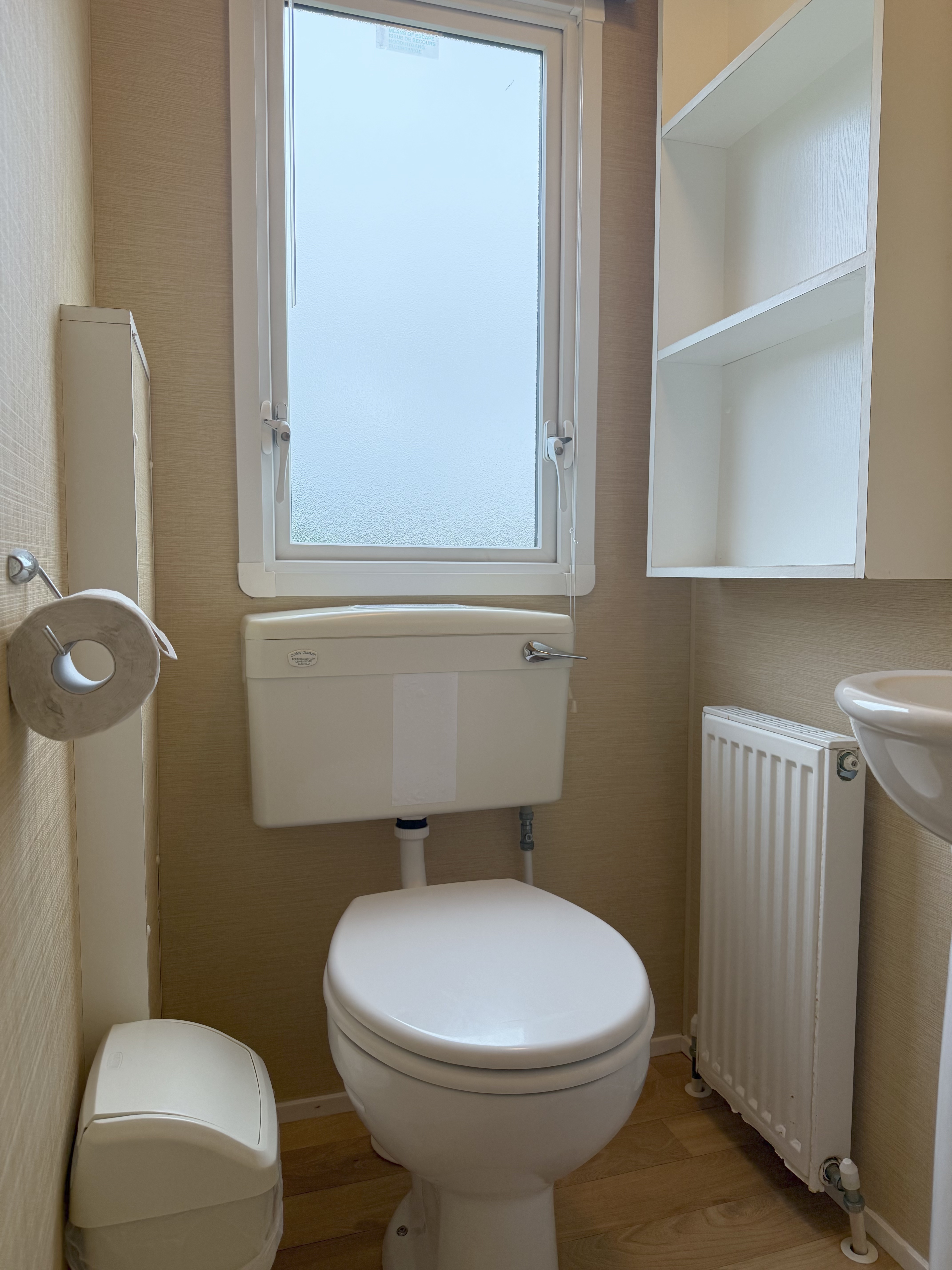 Small bathroom with a toilet, frosted window, wall-mounted storage, and a radiator