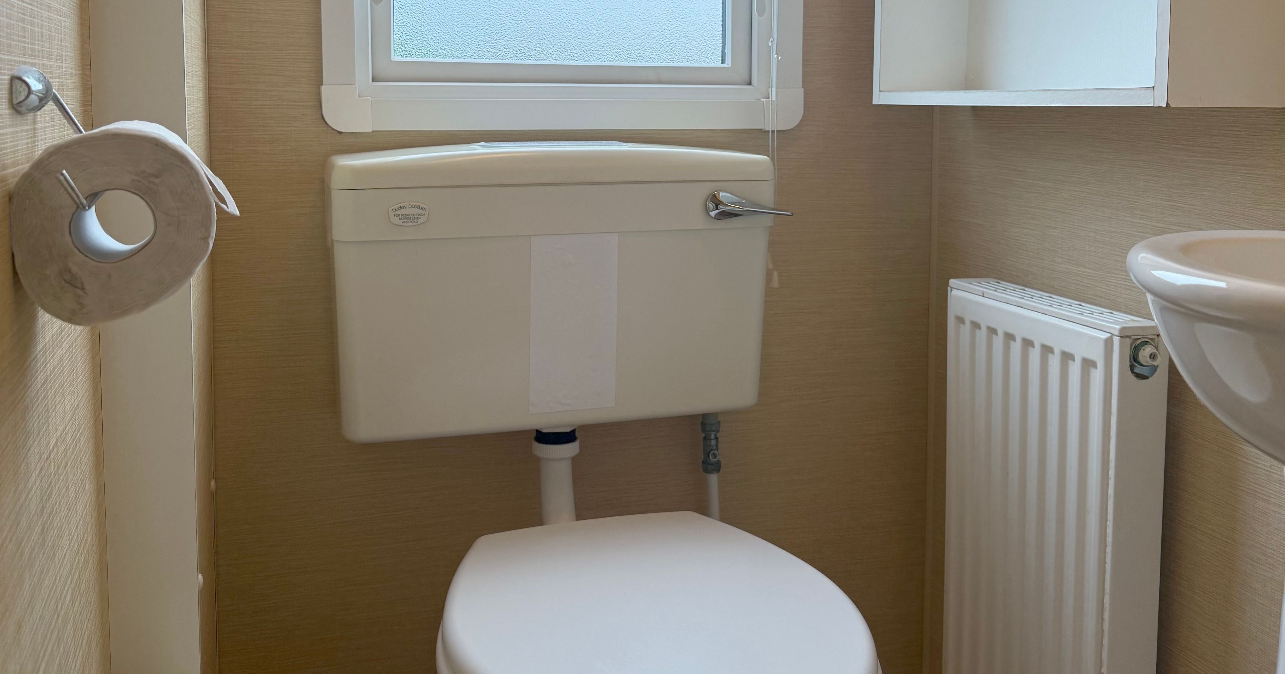 Small bathroom with a toilet, frosted window, wall-mounted storage, and a radiator