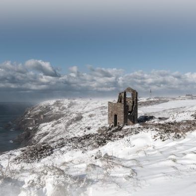 Snow-covered ruins of Wheal Owles and the Crowns on a coastal cliff.