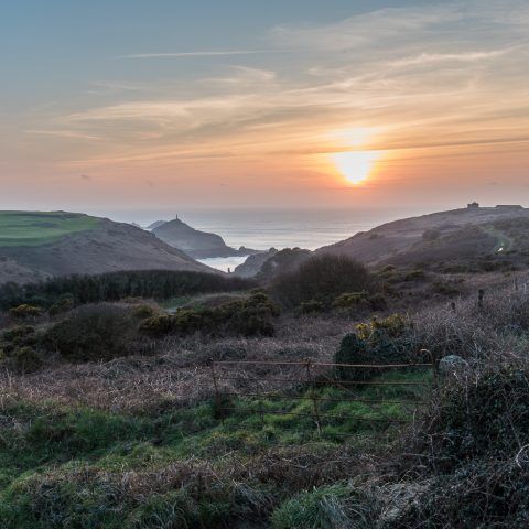 Sunset over Kenidjack Valley with the sun shining over rolling hills and the sea in the distance.