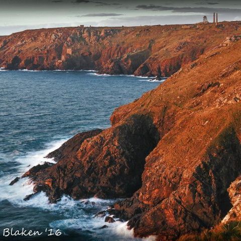 Rocky coastal cliffs at sunset with historic mine buildings on the headland