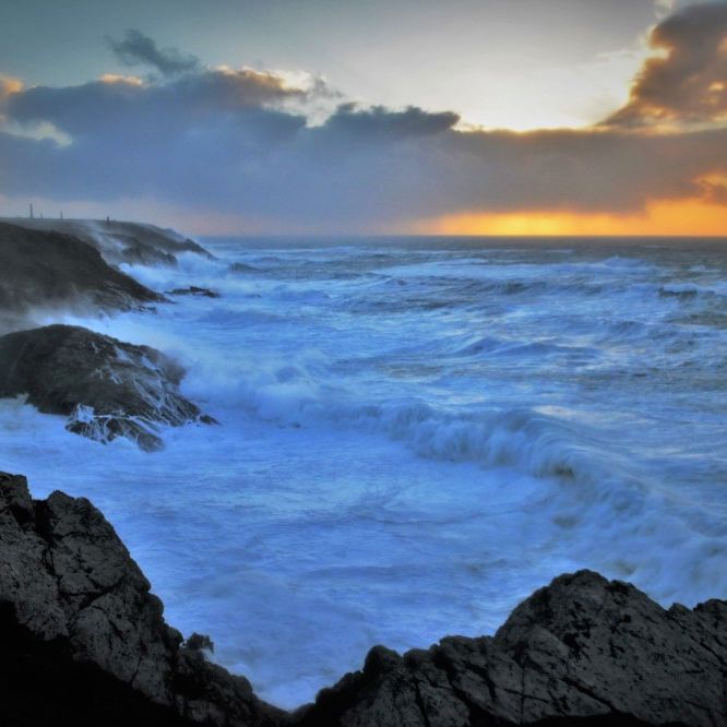 Dramatic ocean waves crashing against rocky coastline at sunset