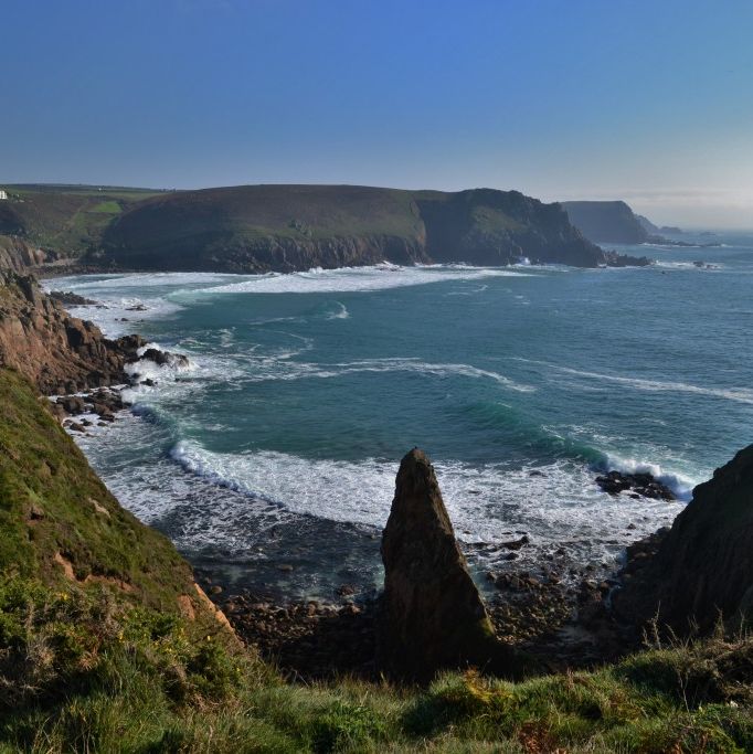 Rocky coastal cliffs with waves crashing against the shore under a clear blue sky.