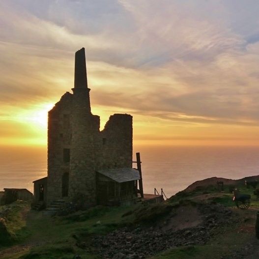 Ruins of an old stone mining building and wooden structures on a coastal landscape at sunset