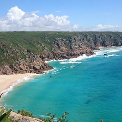 Cliffs and sandy beach on the coast of West Cornwall with turquoise sea and blue sky.
