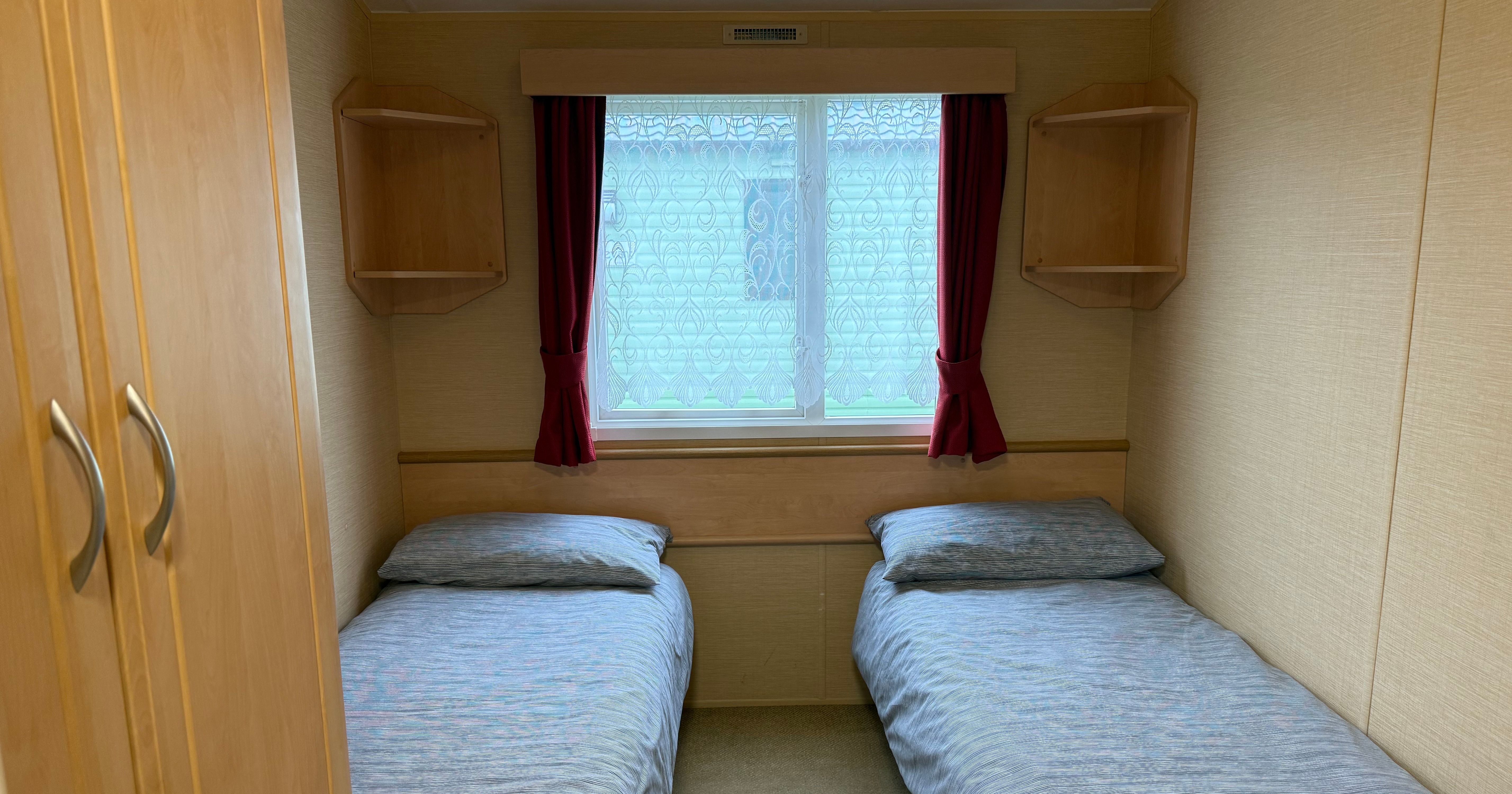 Small bedroom with two single beds and a window with red curtains