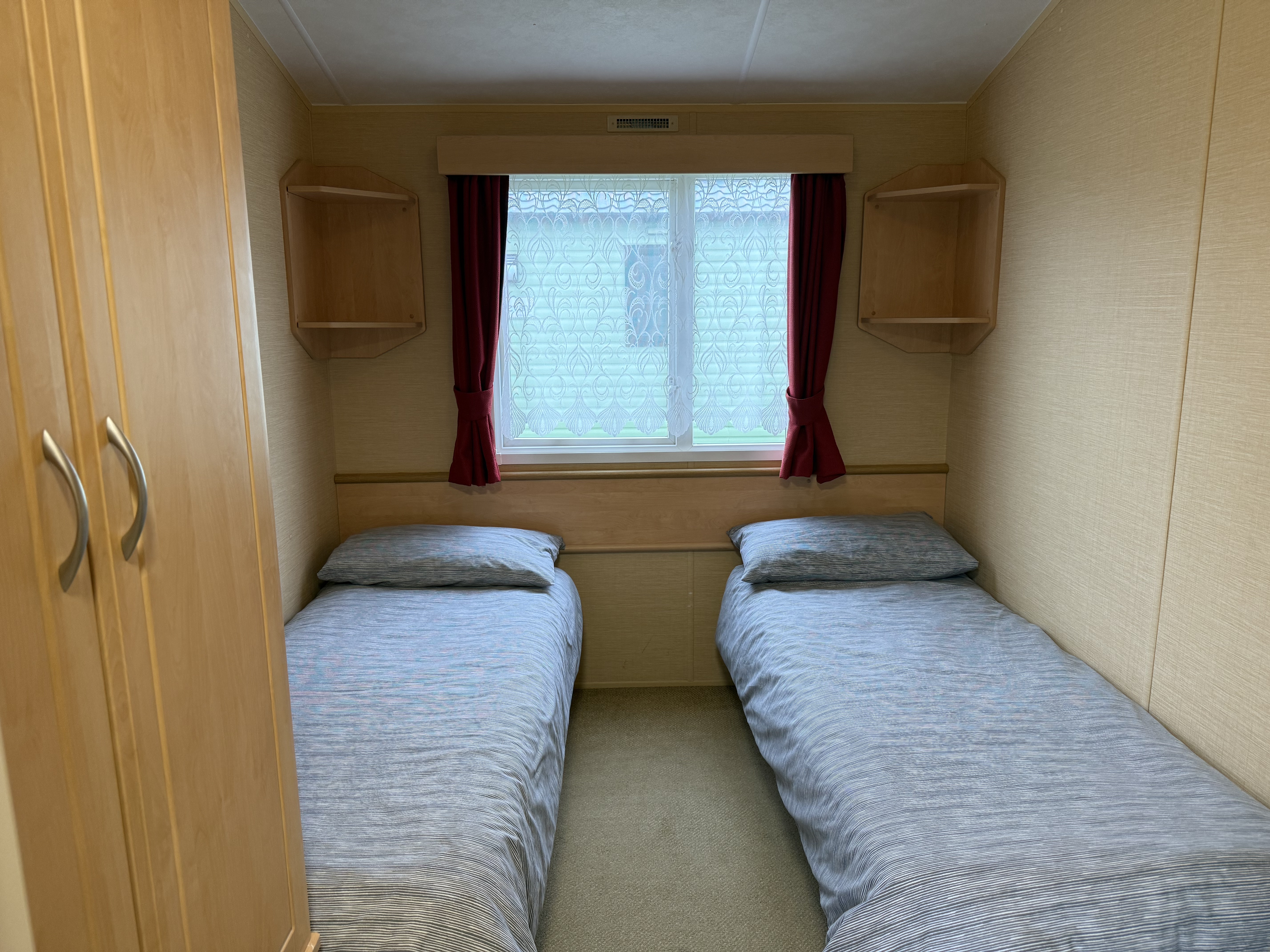 Small bedroom with two single beds and a window with red curtains