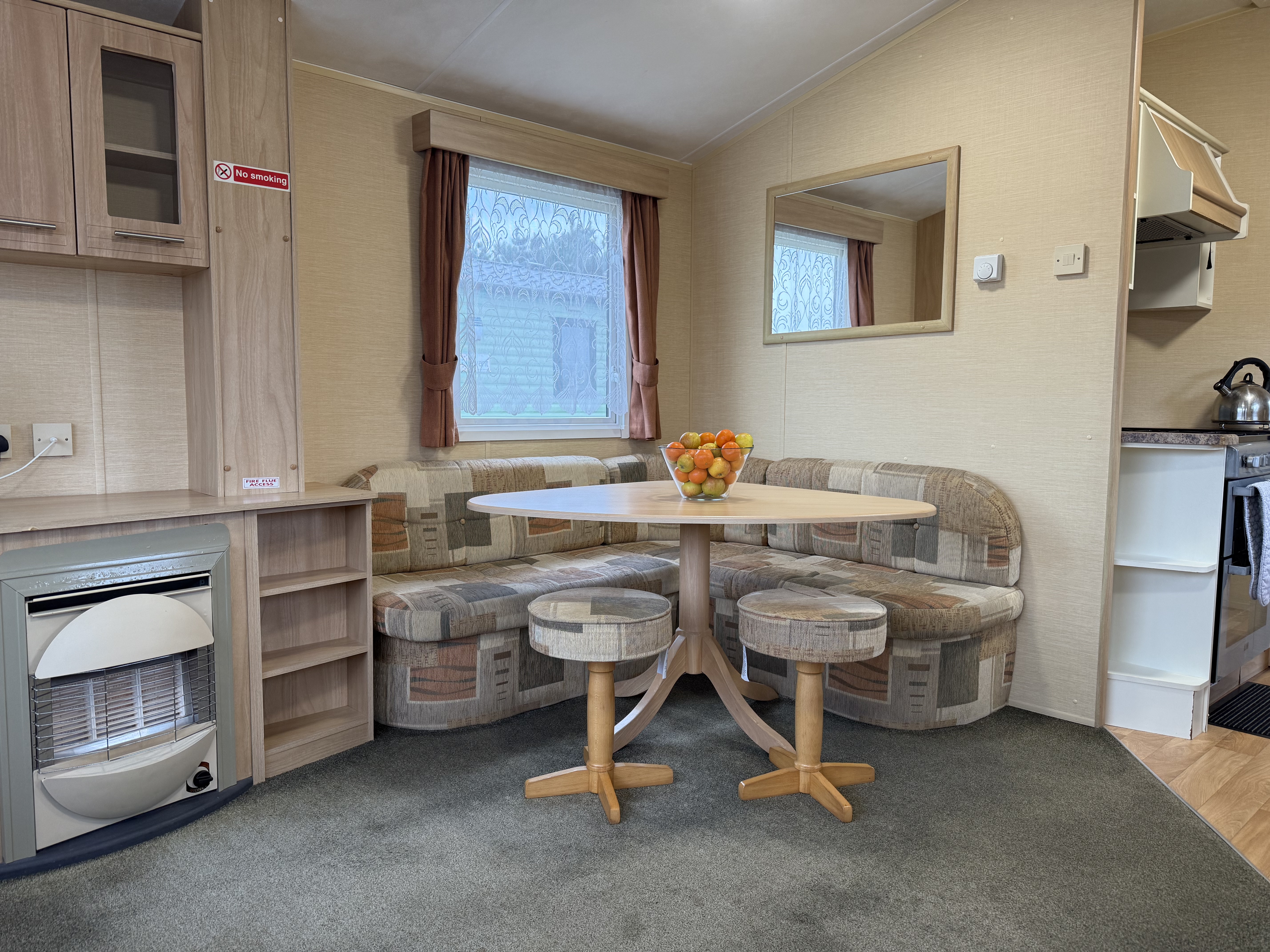 Interior of a cozy caravan or mobile home dining area with a round table, cushioned bench seating, and a bowl of fruit.