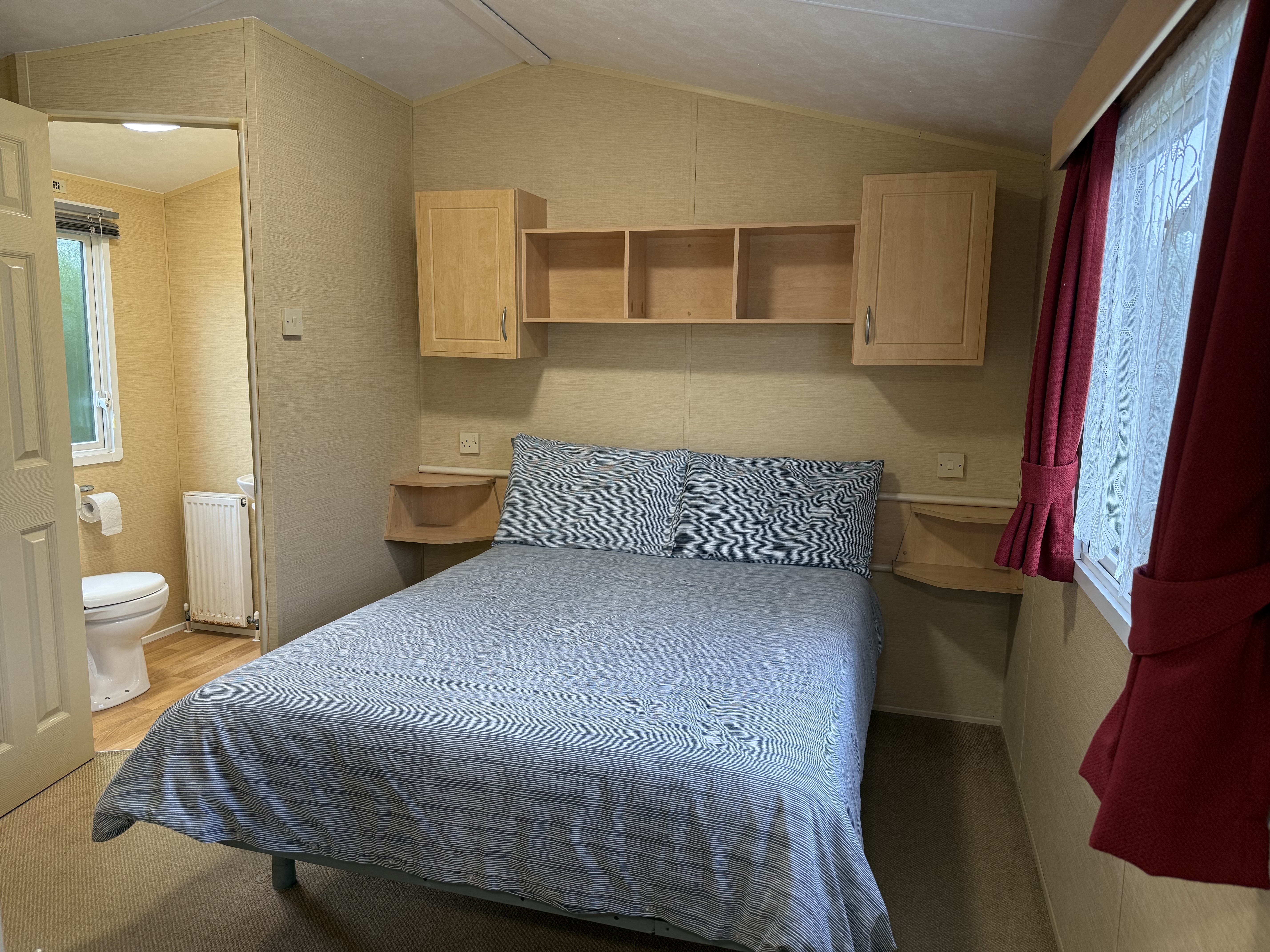 Small bedroom with double bed, attached bathroom, and red curtains