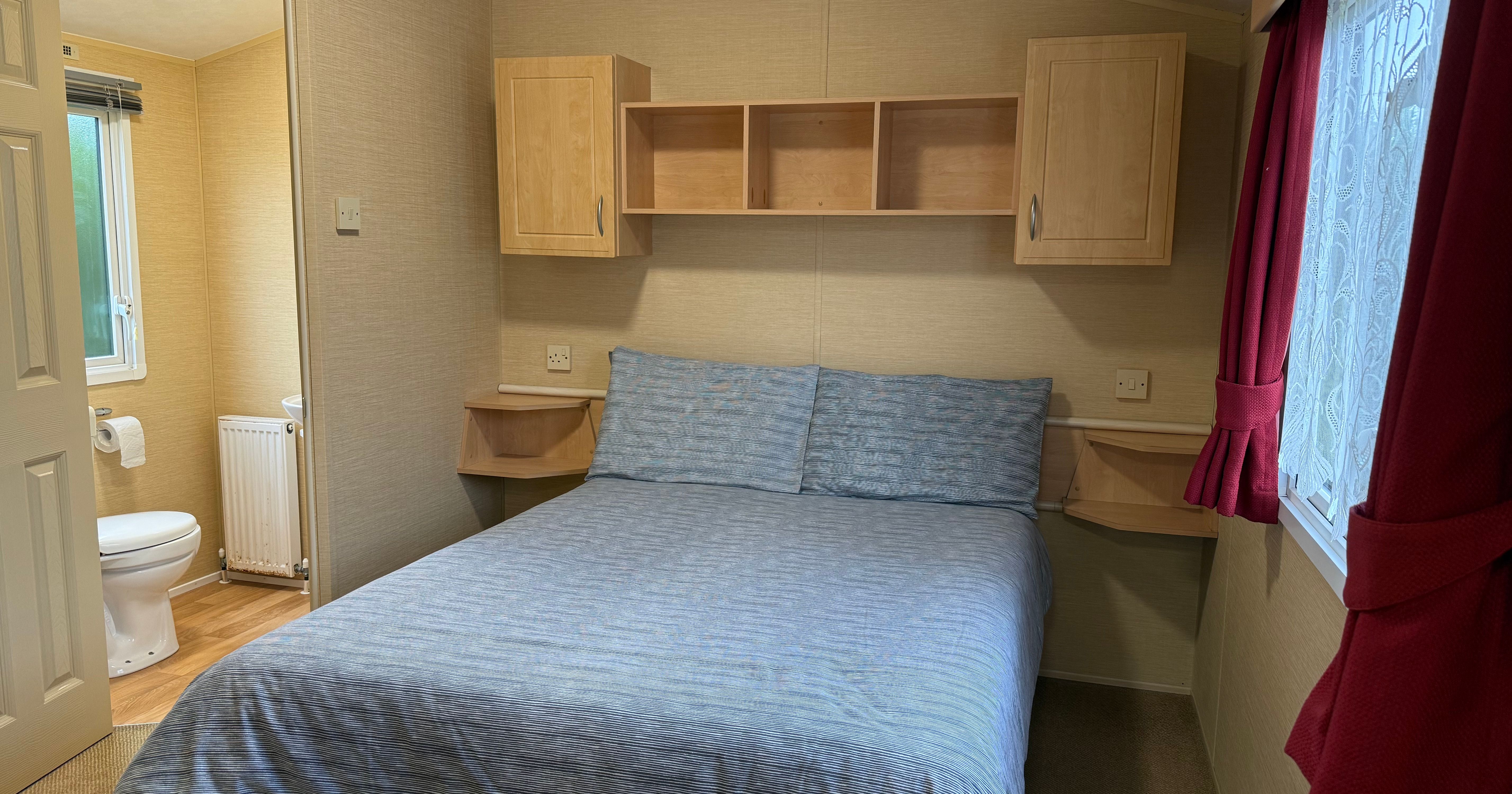 Small bedroom with double bed, attached bathroom, and red curtains