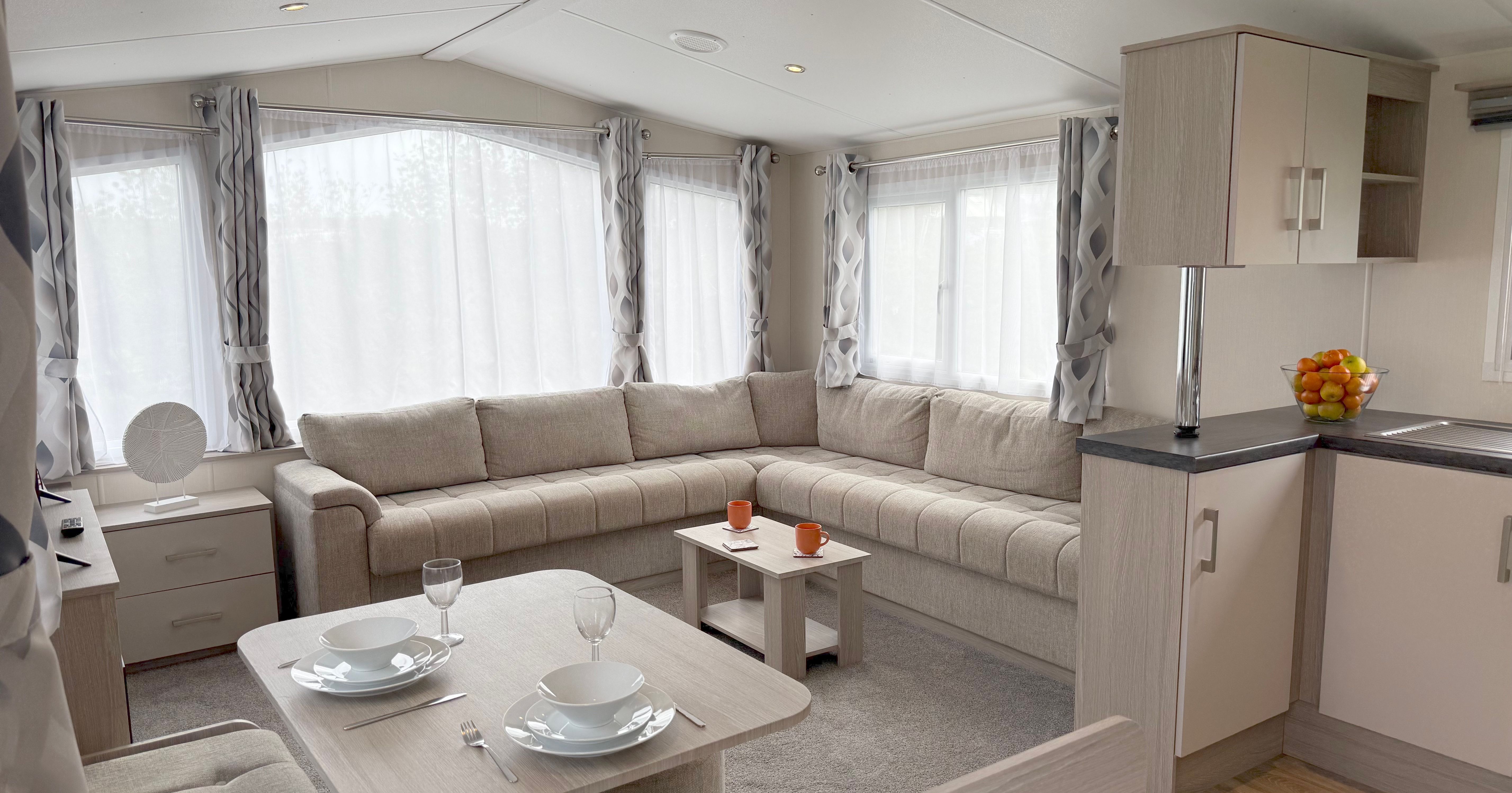 Modern caravan interior with large beige sofa, dining area, and kitchenette