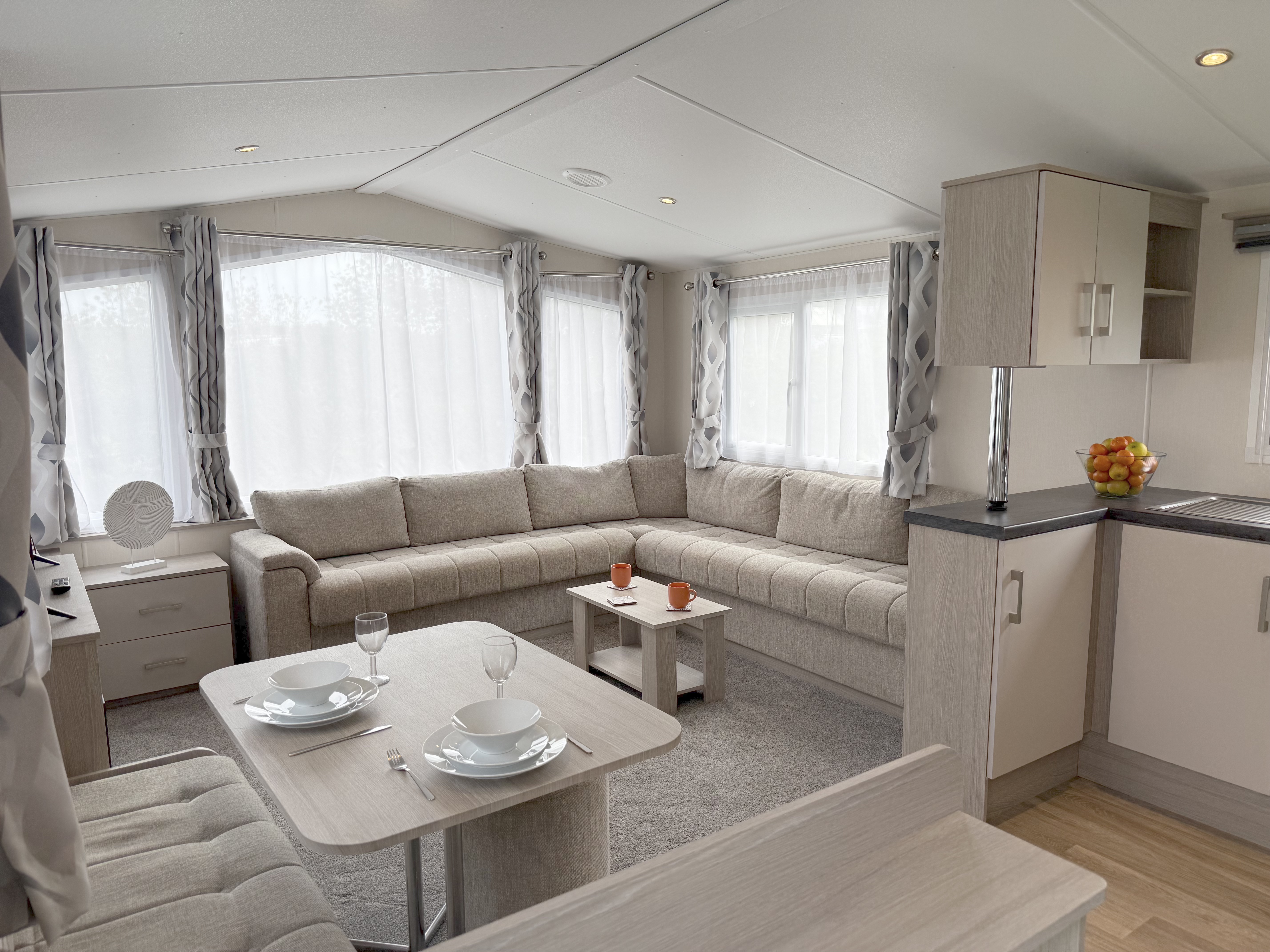 Modern caravan interior with large beige sofa, dining area, and kitchenette