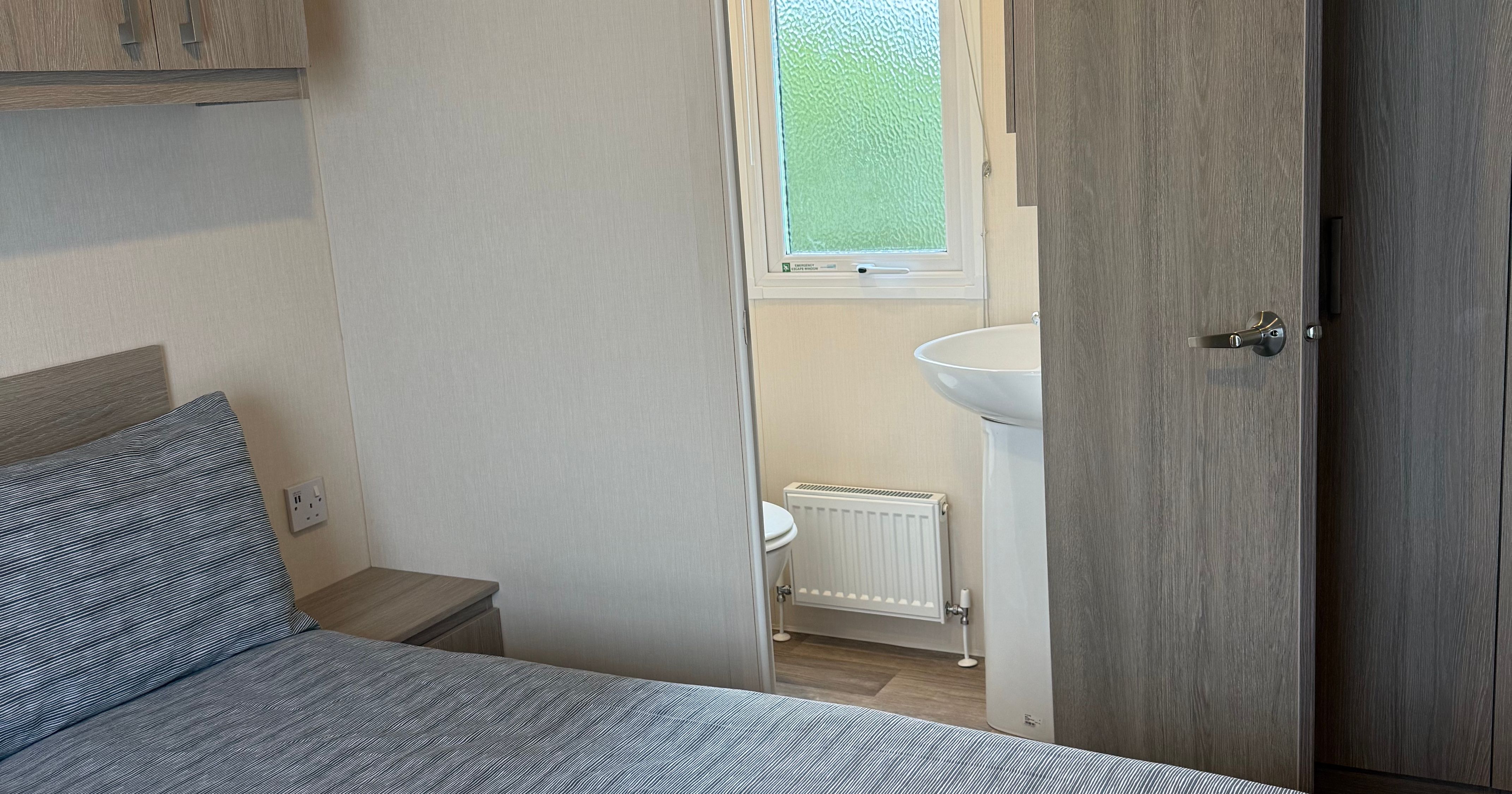 A modern bedroom with a neatly made bed and an open door revealing a small bathroom.