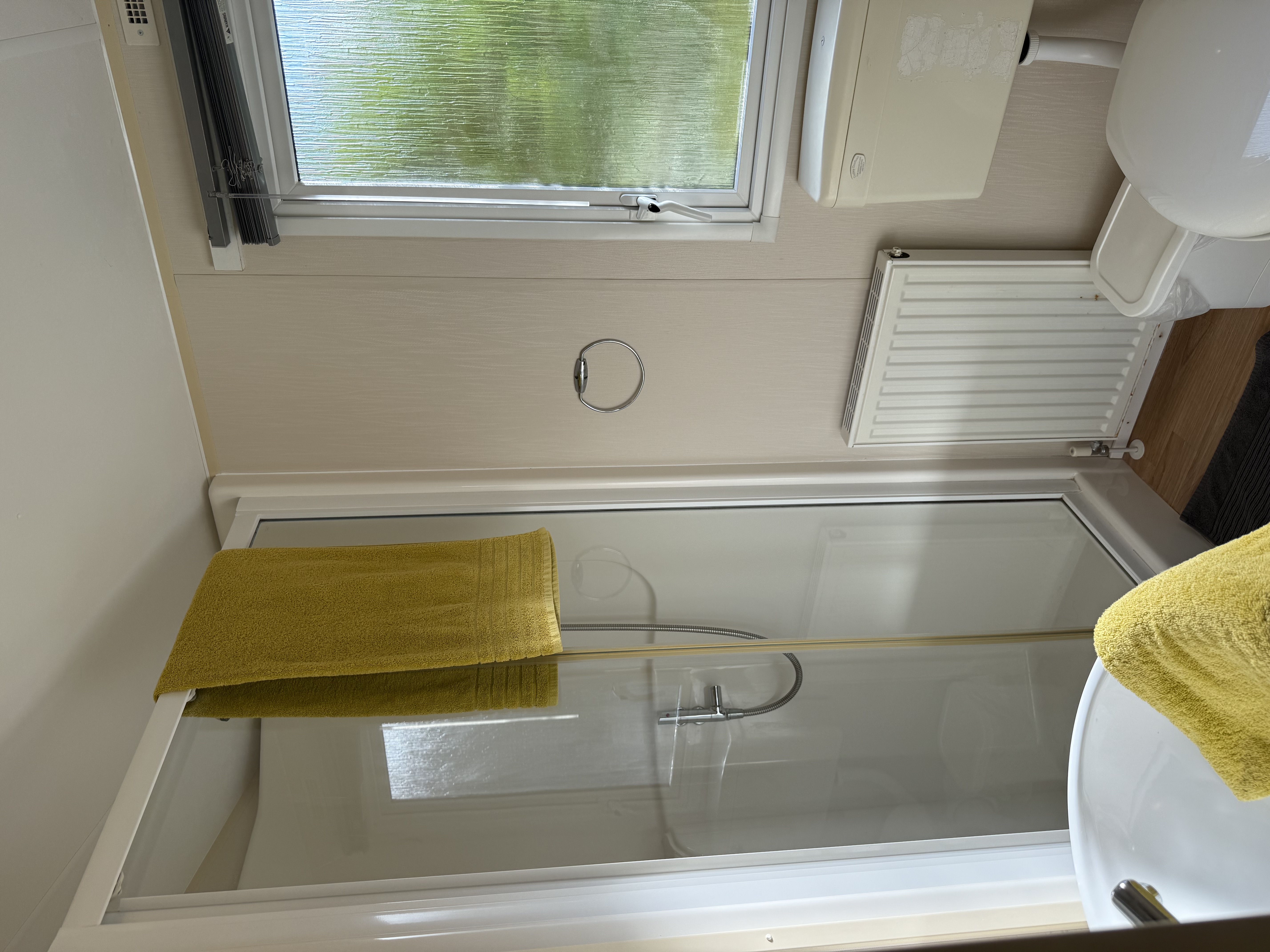 Compact bathroom with shower, toilet, towel, sink and window